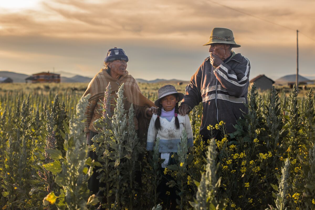 A man and woman stand on either side of a young girl with their hands on her shoulders. They are in a field.