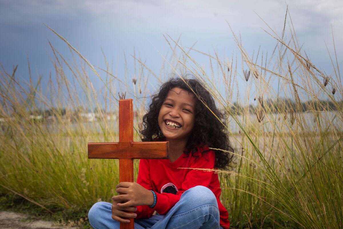 A girl in a red sweater holds a wooden cross and smiles