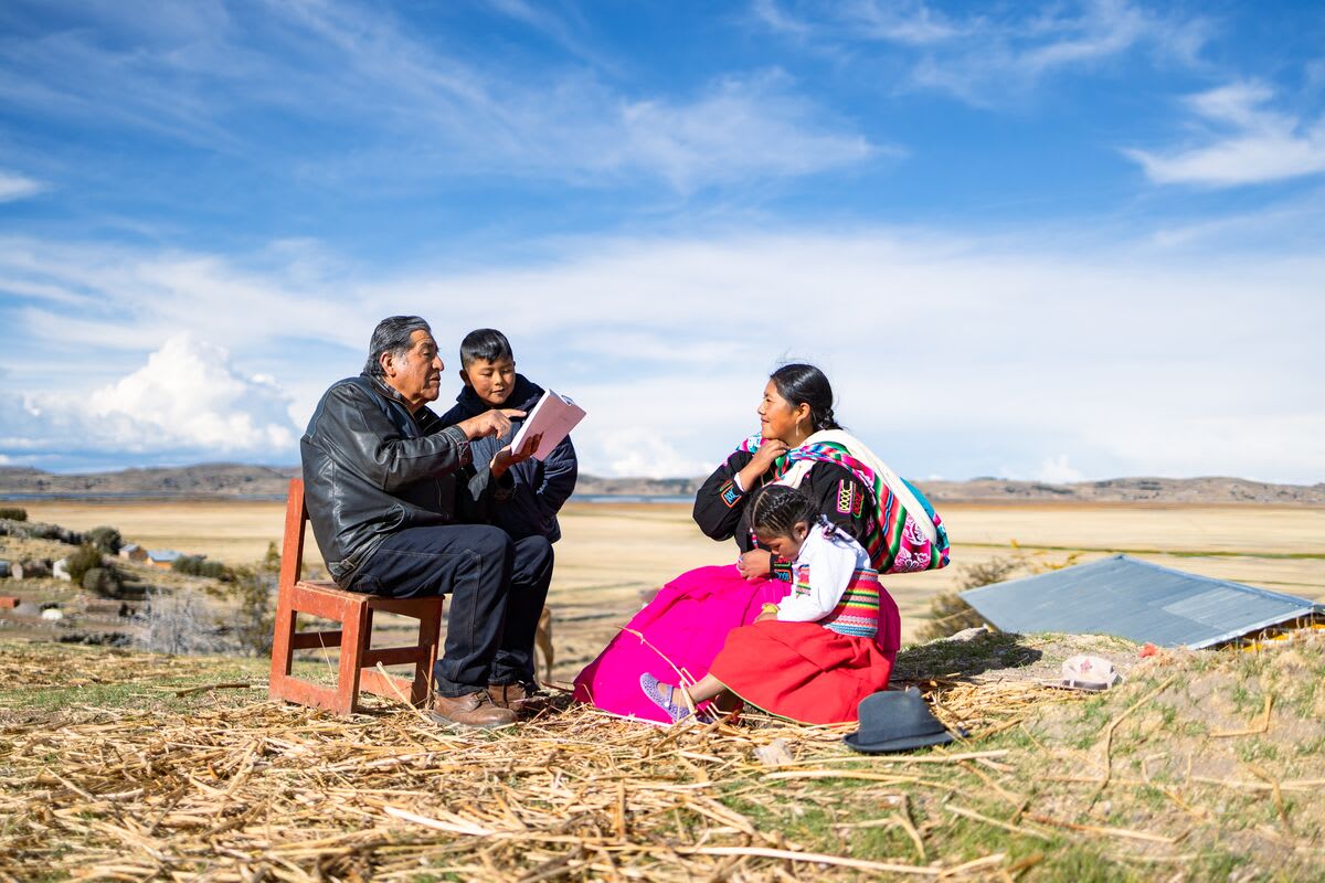 A family sits around a man reading