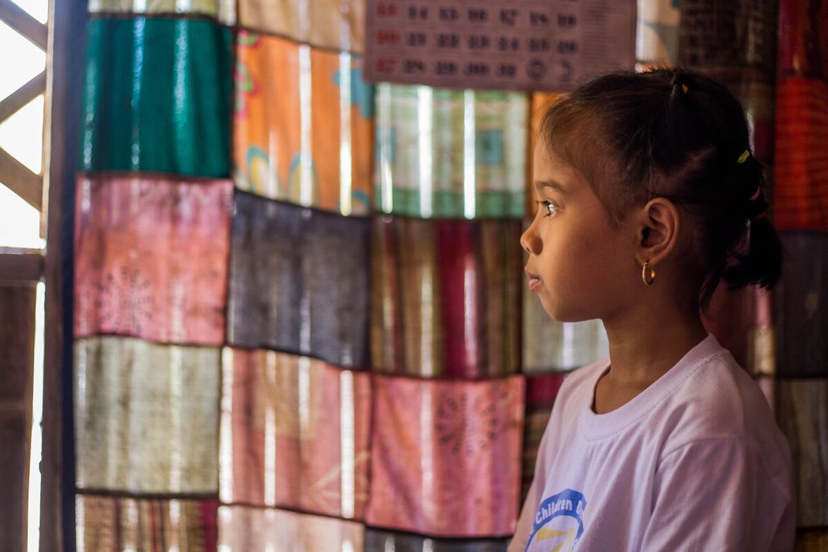 A girl stands before a patchwork curtain and looks ahead