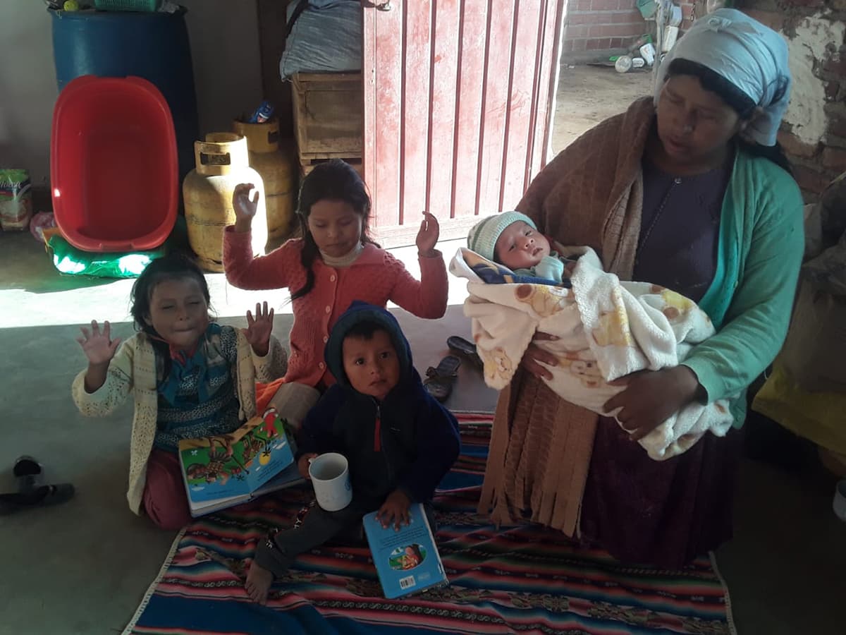 A Bolivian woman kneels down and prays. She holds a young baby and three other children kneel and pray beside her.