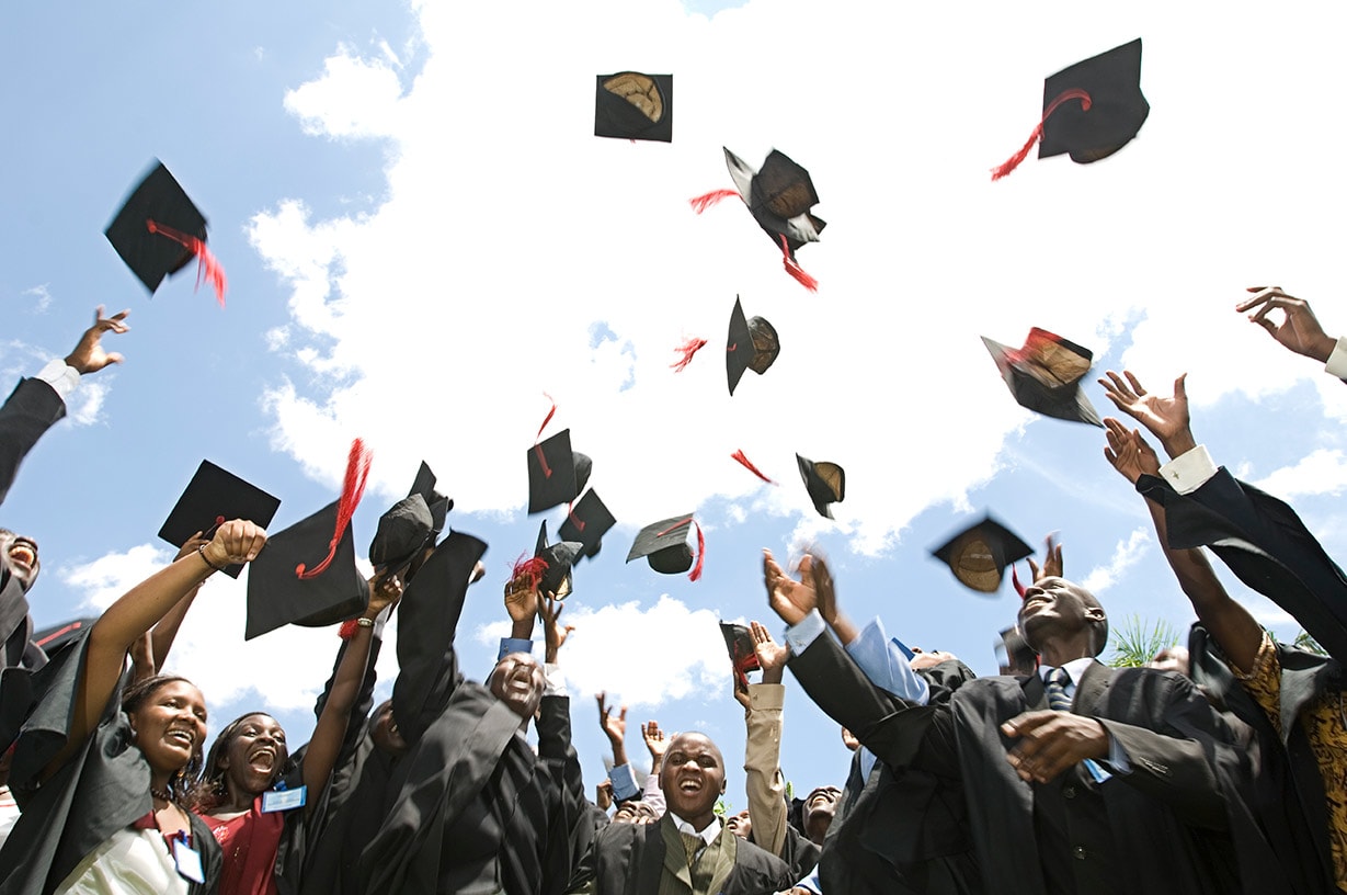 Graduates in Uganda wearing robes throw their graduation caps in the air.