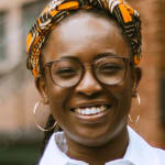 A woman in a white shirt stands smiling at the camera with her hand in her pocket