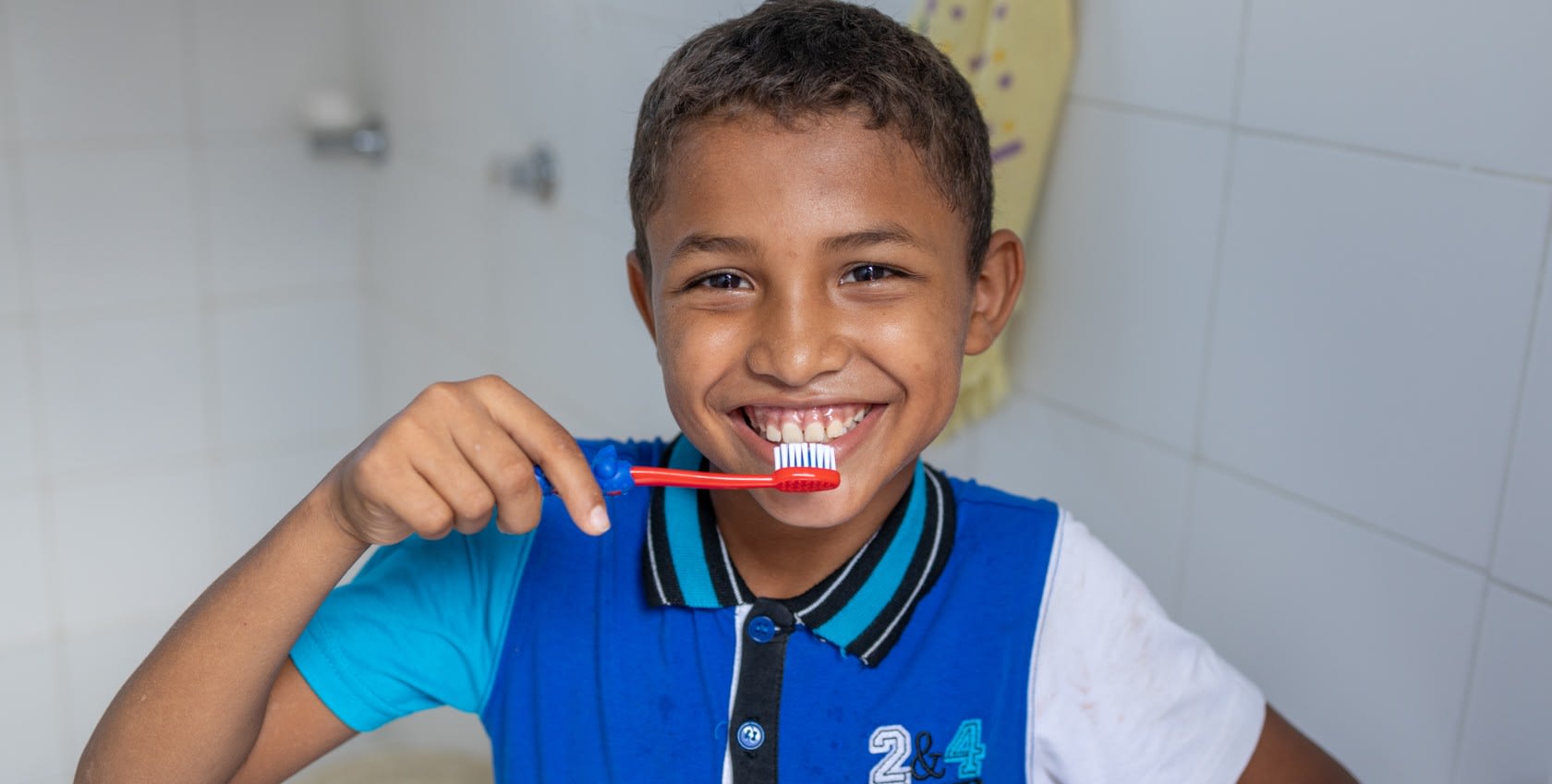 A boy holding tooth brush brushing his teeth with a smile on his face
