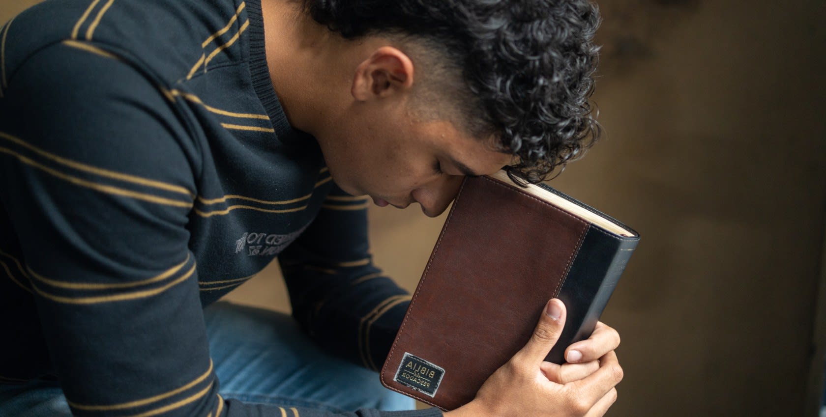 A young man praying with a bible in his hand.