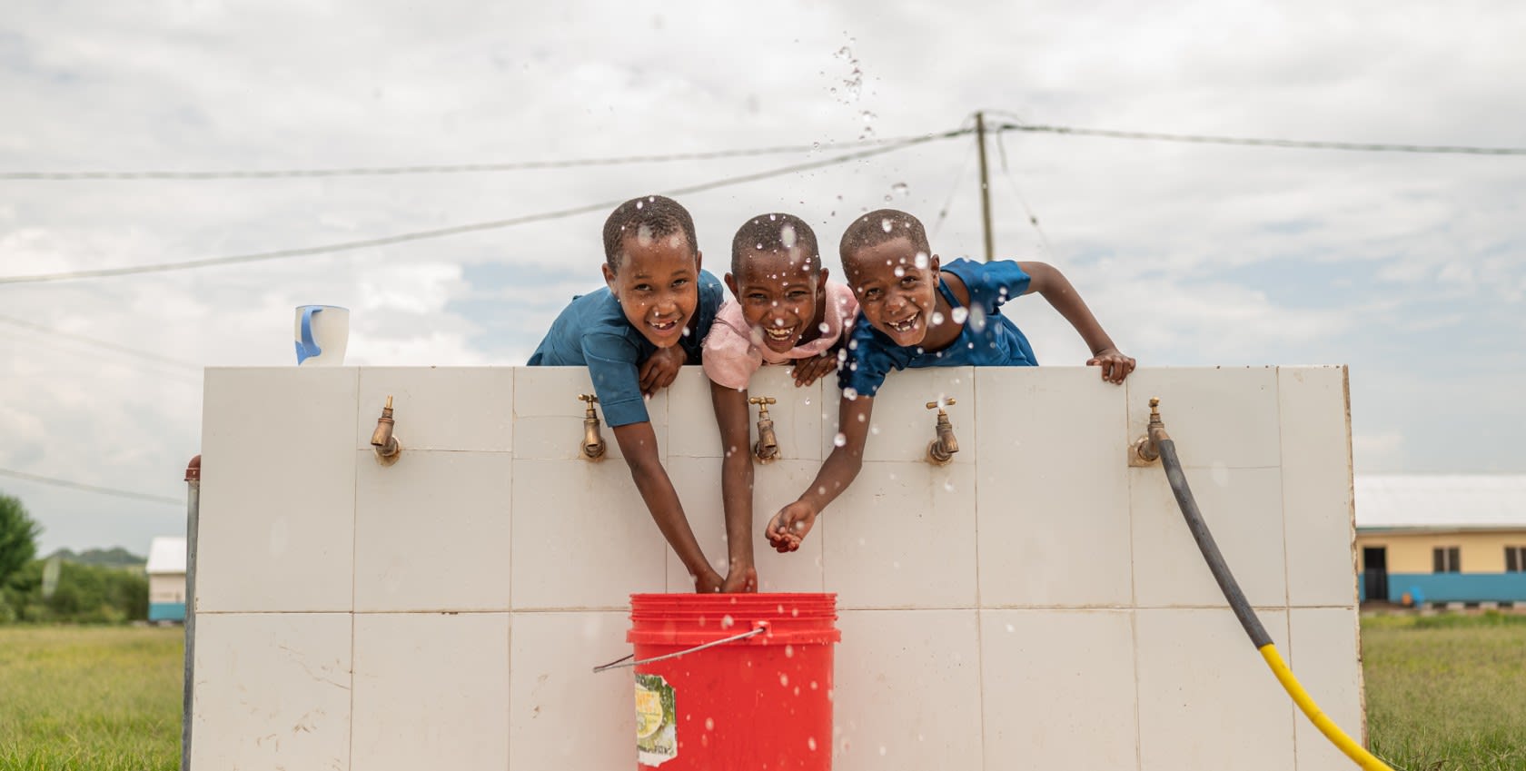 3 children happily getting access to a red bucket of water