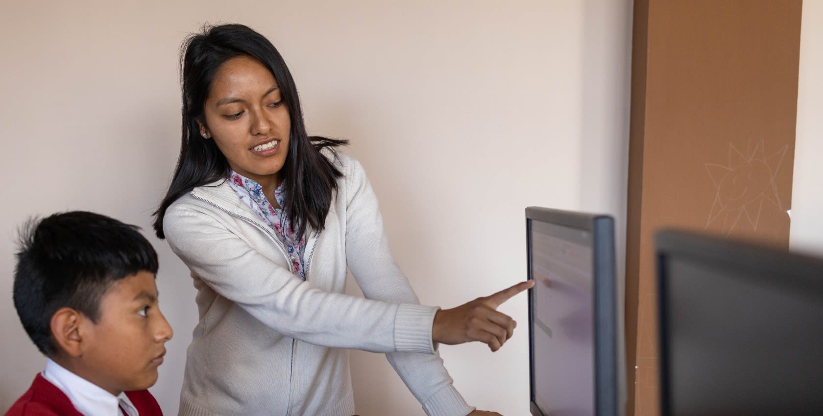 A female teacher teaching a young boy how to use a computer.
