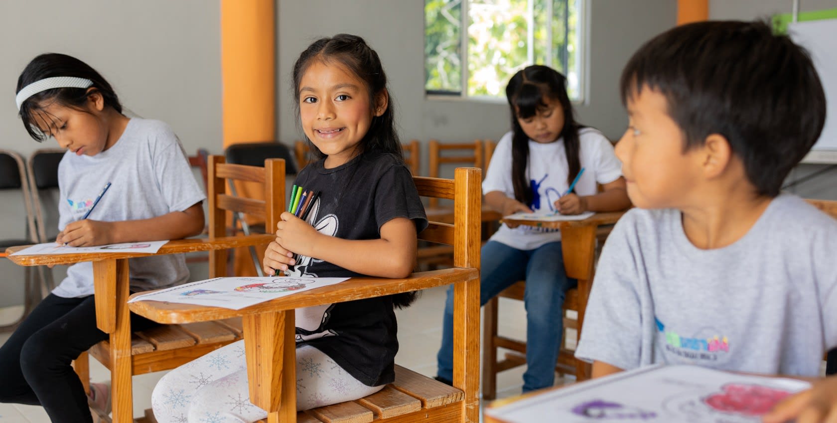 A young girl sitting in a classroom with her classmates, drawing together.
