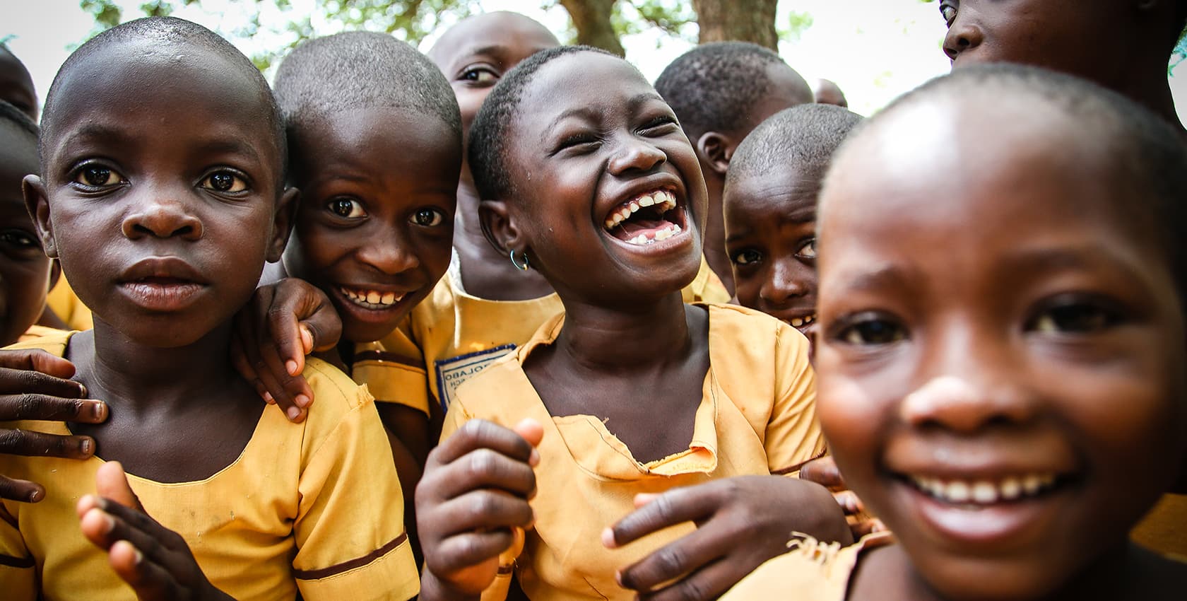 A group of children in yellow, school uniforms smile and laugh