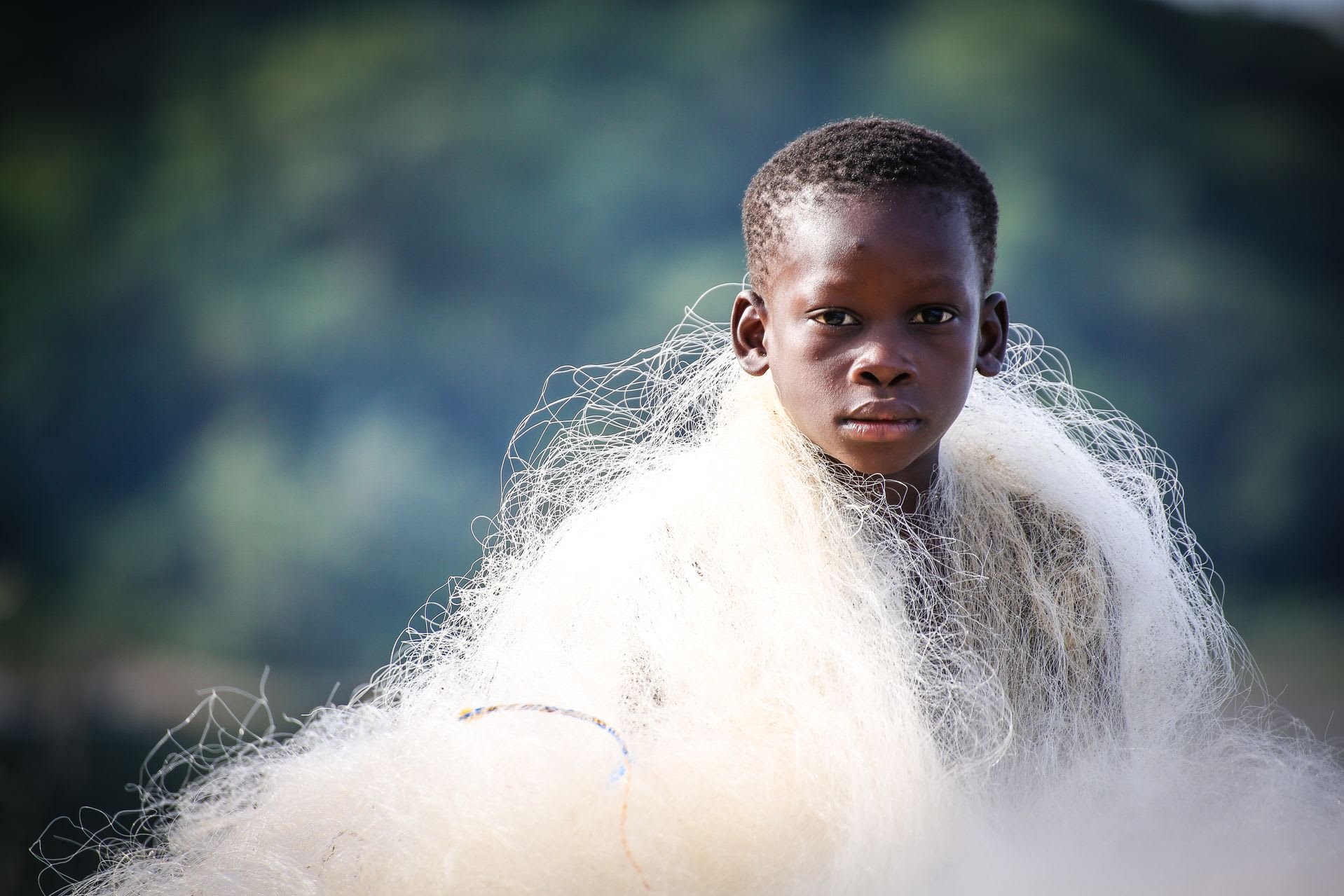 A boy has a white fishing net wrapped around his shoulders. The background is blurry.
