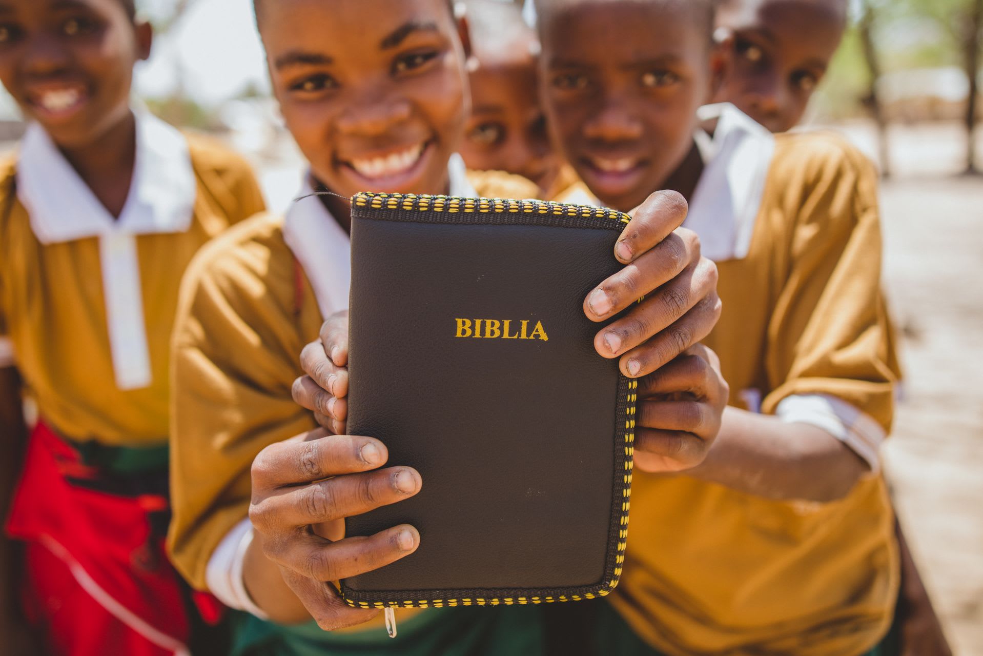 Two smiling children in Tanzania hold up a brown and yellow Bible.