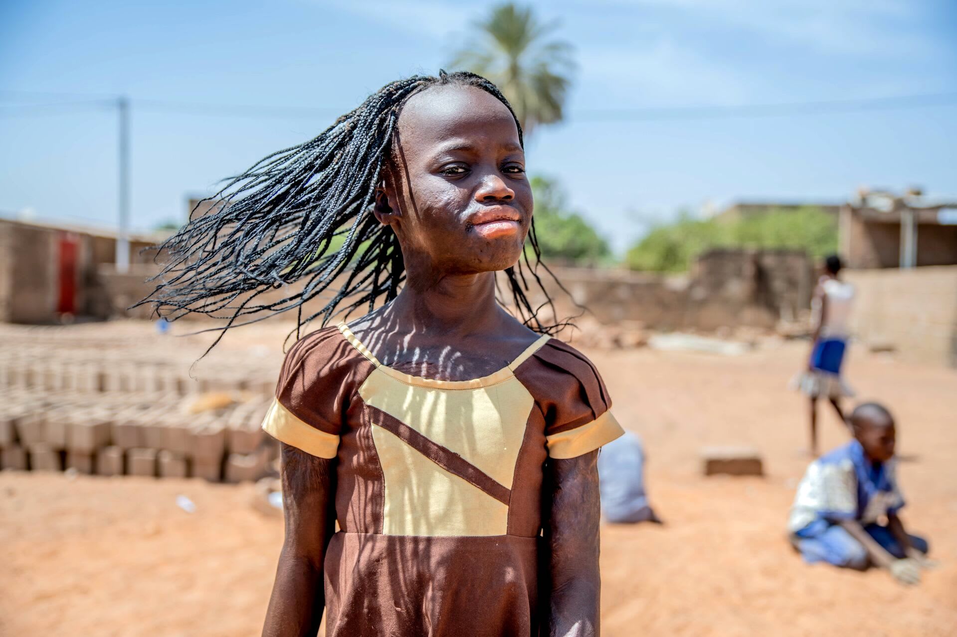 Girl wearing a brown dress turns her head and looks at the camera with confidence. Her hair is flowing in the wind.
