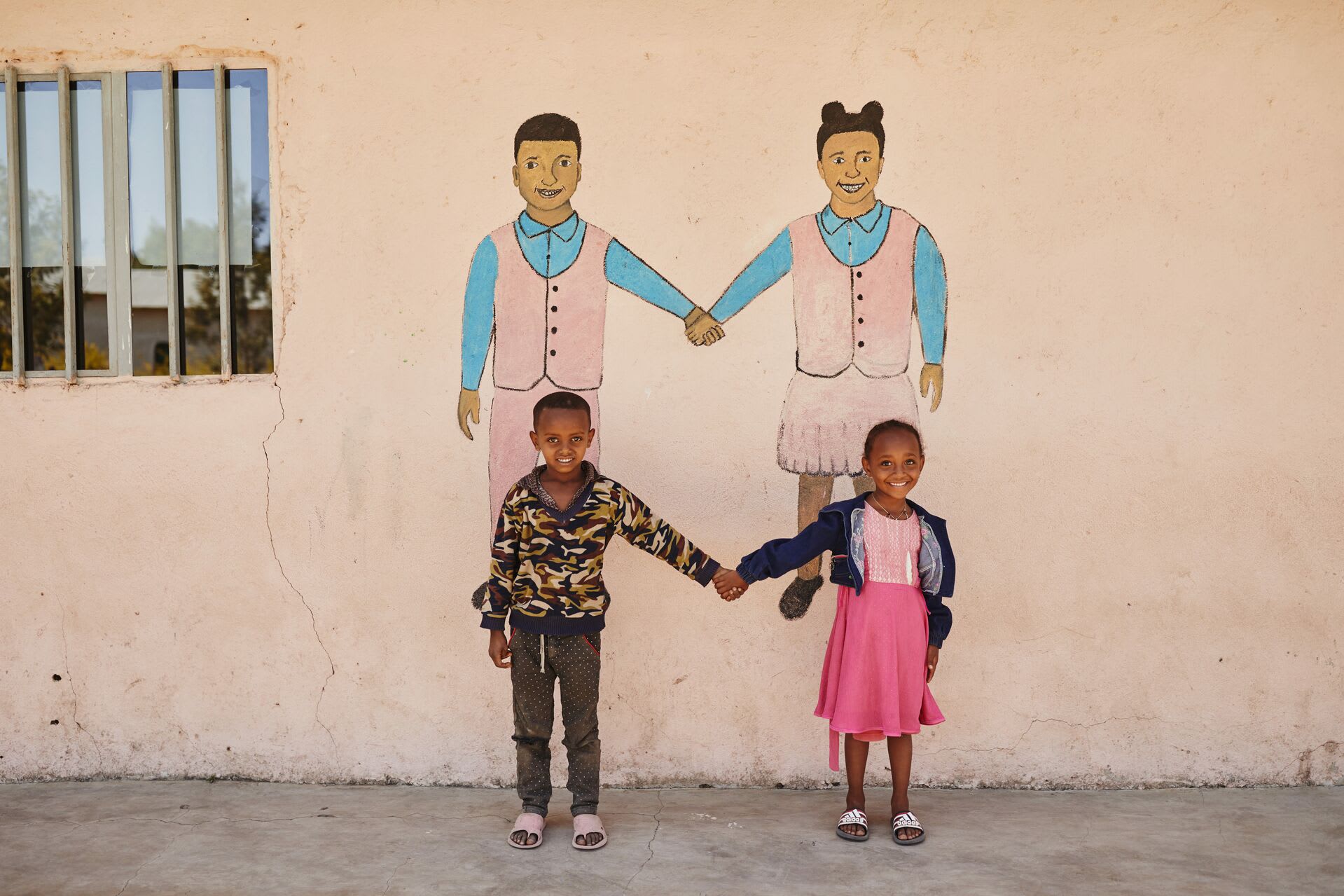 Boy and girl hold hands in font of a mural of a boy and a girl holding hands
