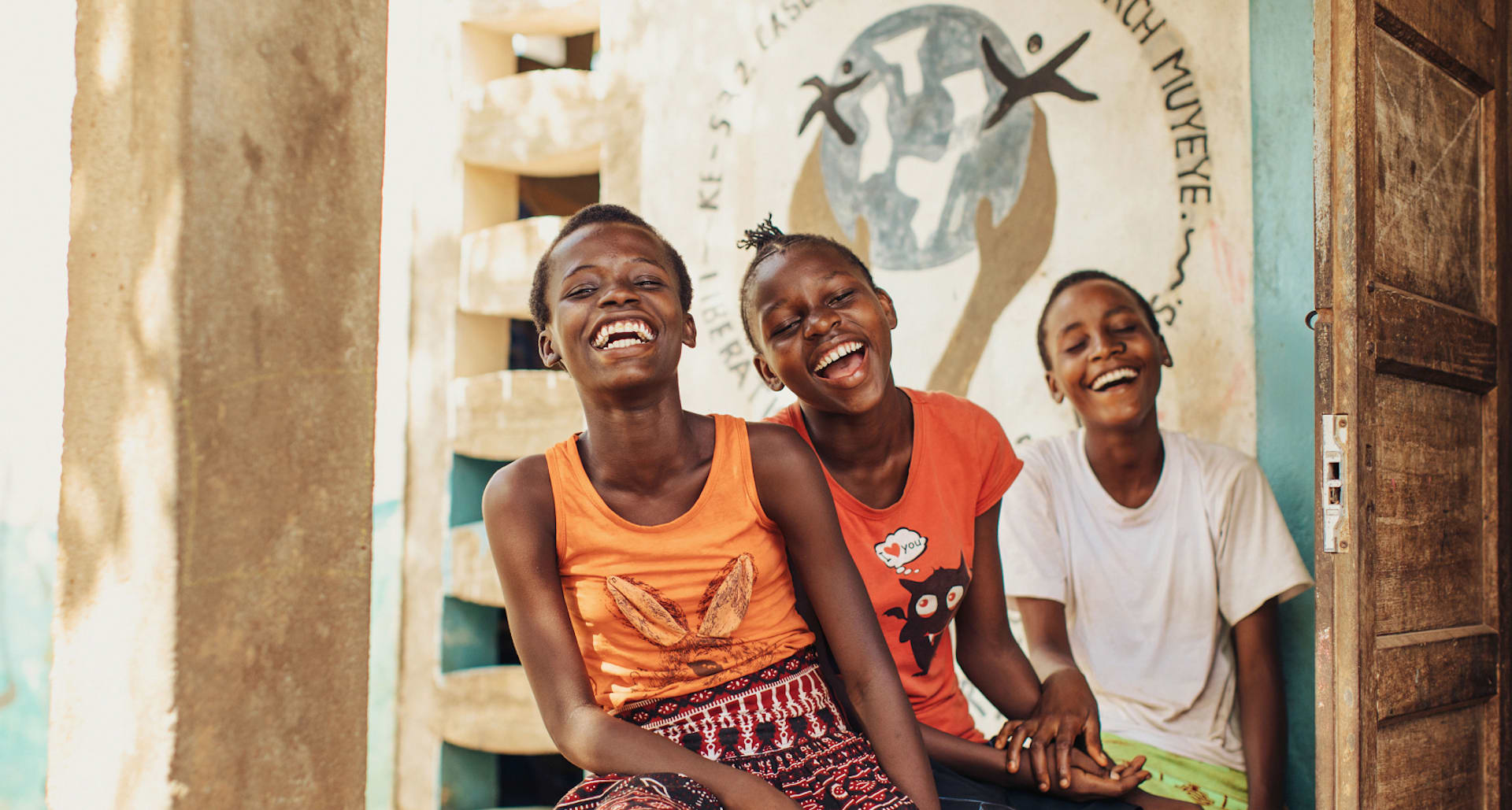 Three teenage girls in Kenya laughing and sitting on the steps of a local church.