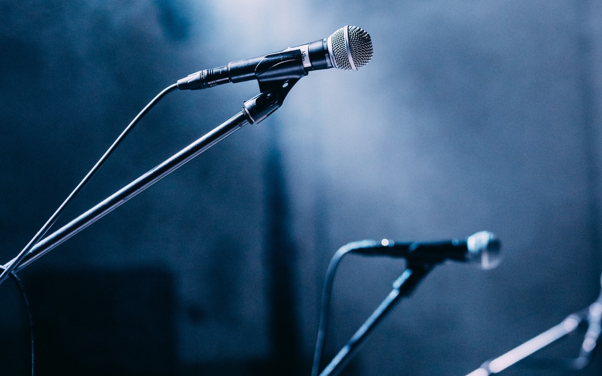 Three wired microphones on a stage against a blurred and foggy background.