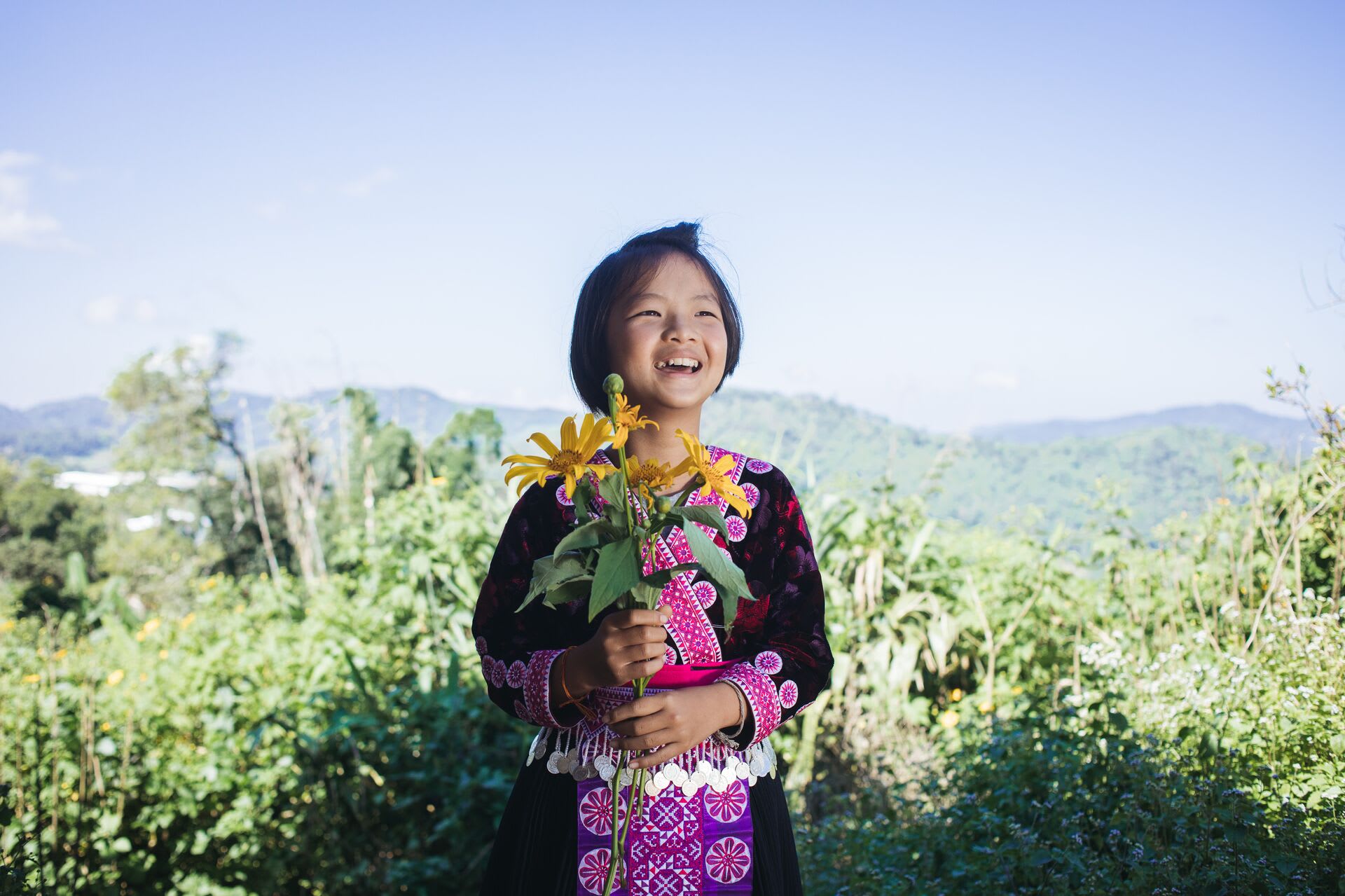 Girl smiles in a field and holds a bouquet of flowers.