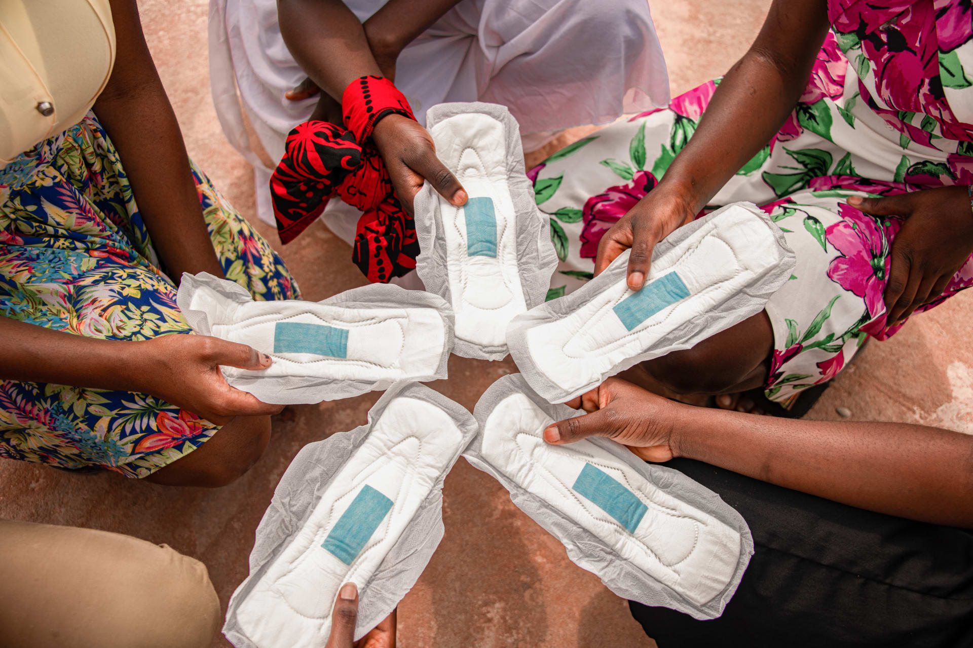 Five girls each hold a sanitary napkin together in a circle for Menstrual Health Day