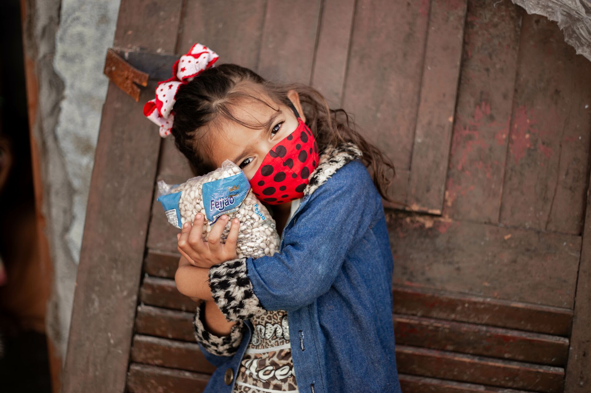 Little girl wears a red mask and hugs a bag of beans