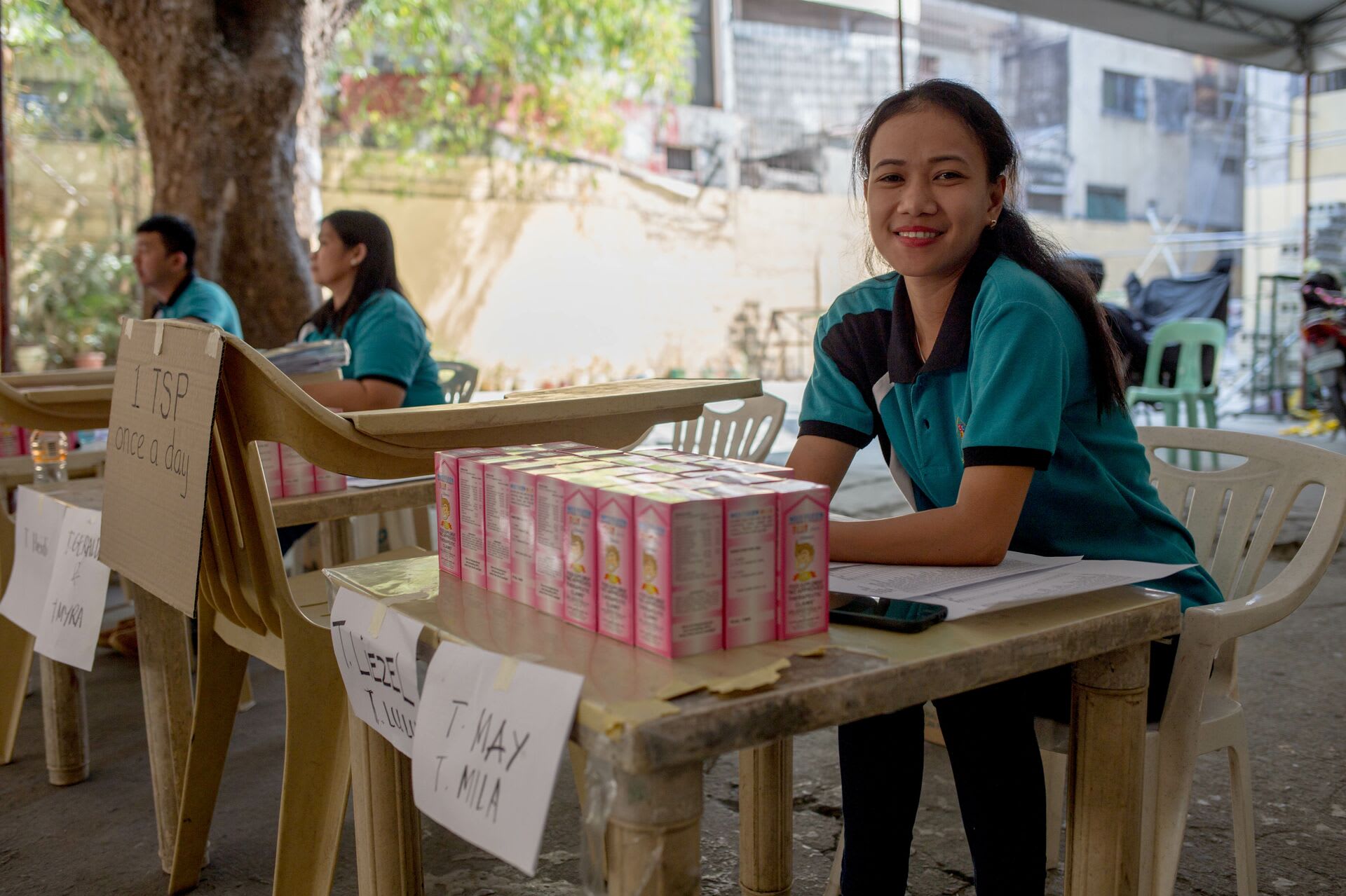 A Compassion Centre staff member sits at a table with packs of vitamins in front of her, ready to distribute to Compassion-assisted families.