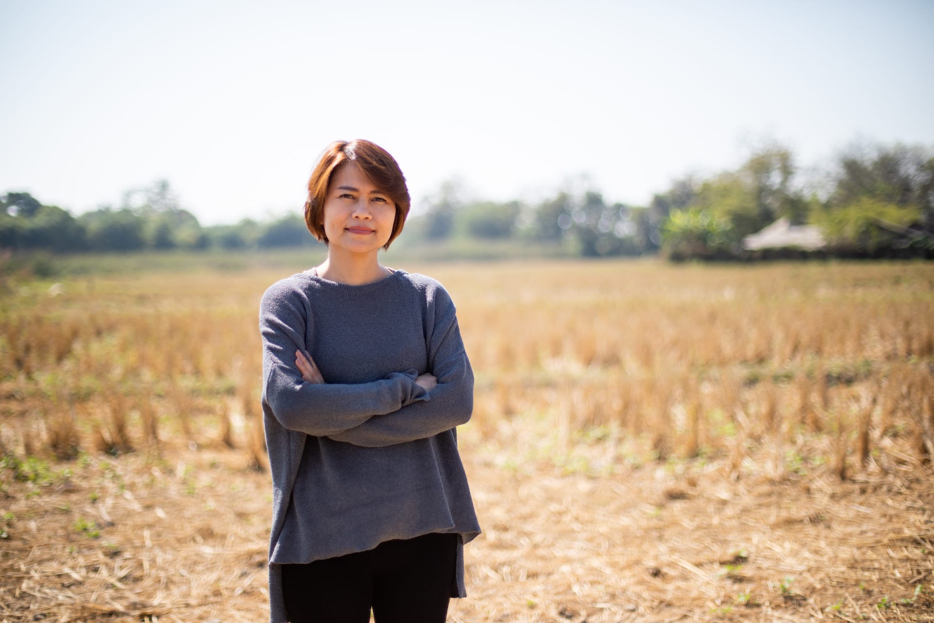 Kriddanchalee, Compassion Thailand's Senior Manager of Program Support, is wearing a gray shirt and is standing on a rice paddy.