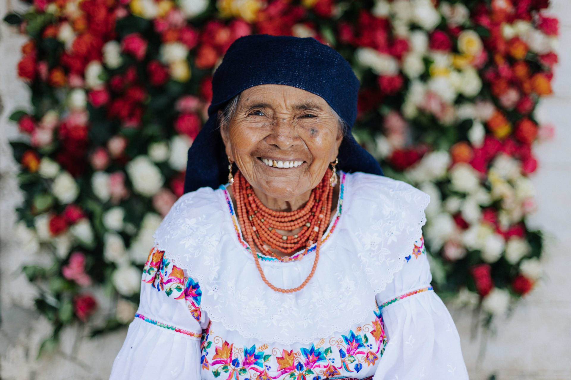 Woman smiles with a floral shirt and orange beads around her neck.