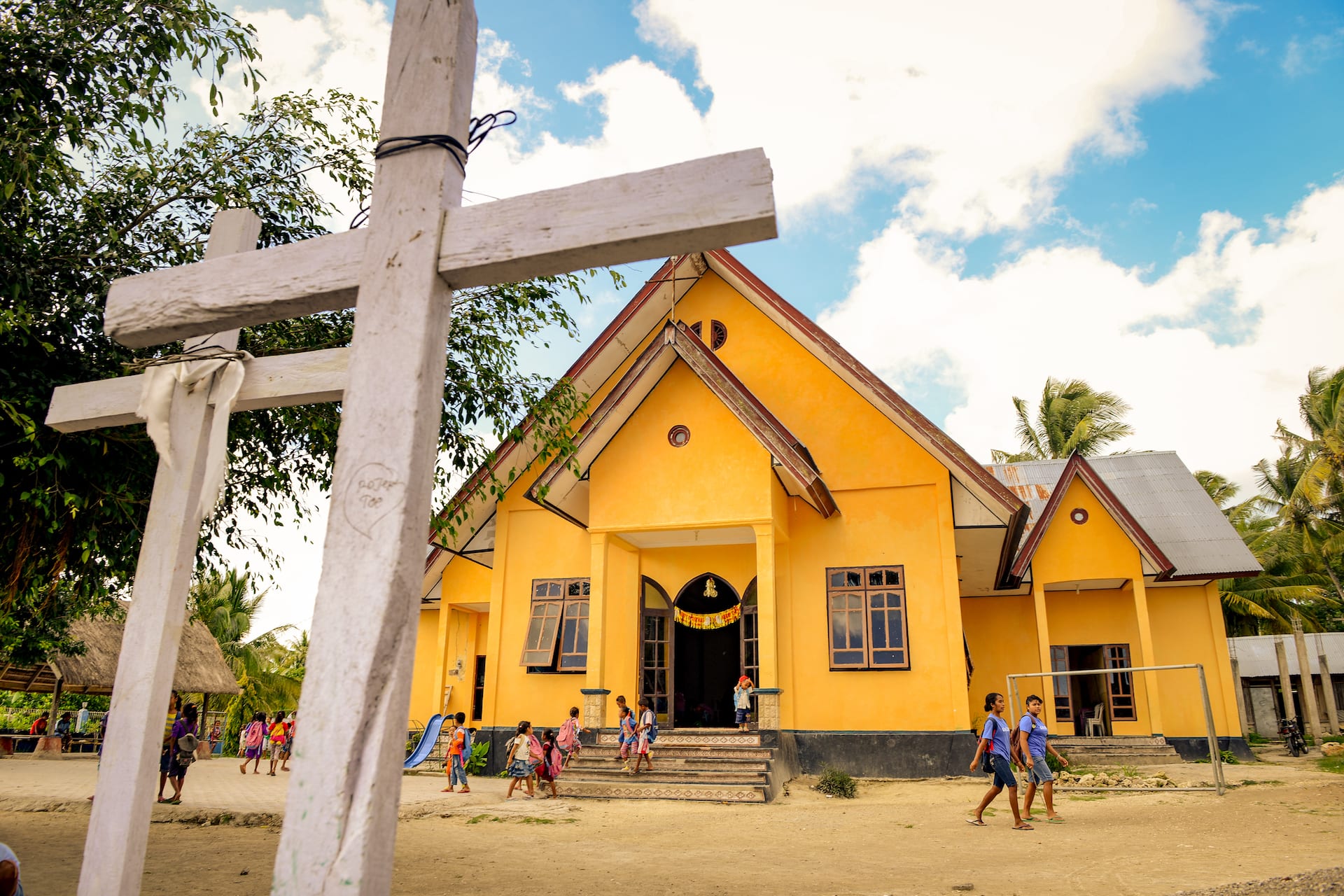 A yellow church building stands behind two wooden crosses under a blue sky.