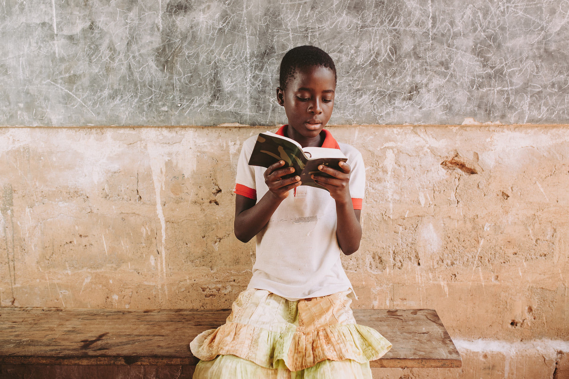 Girl holds a bible and is sitting on a bench.