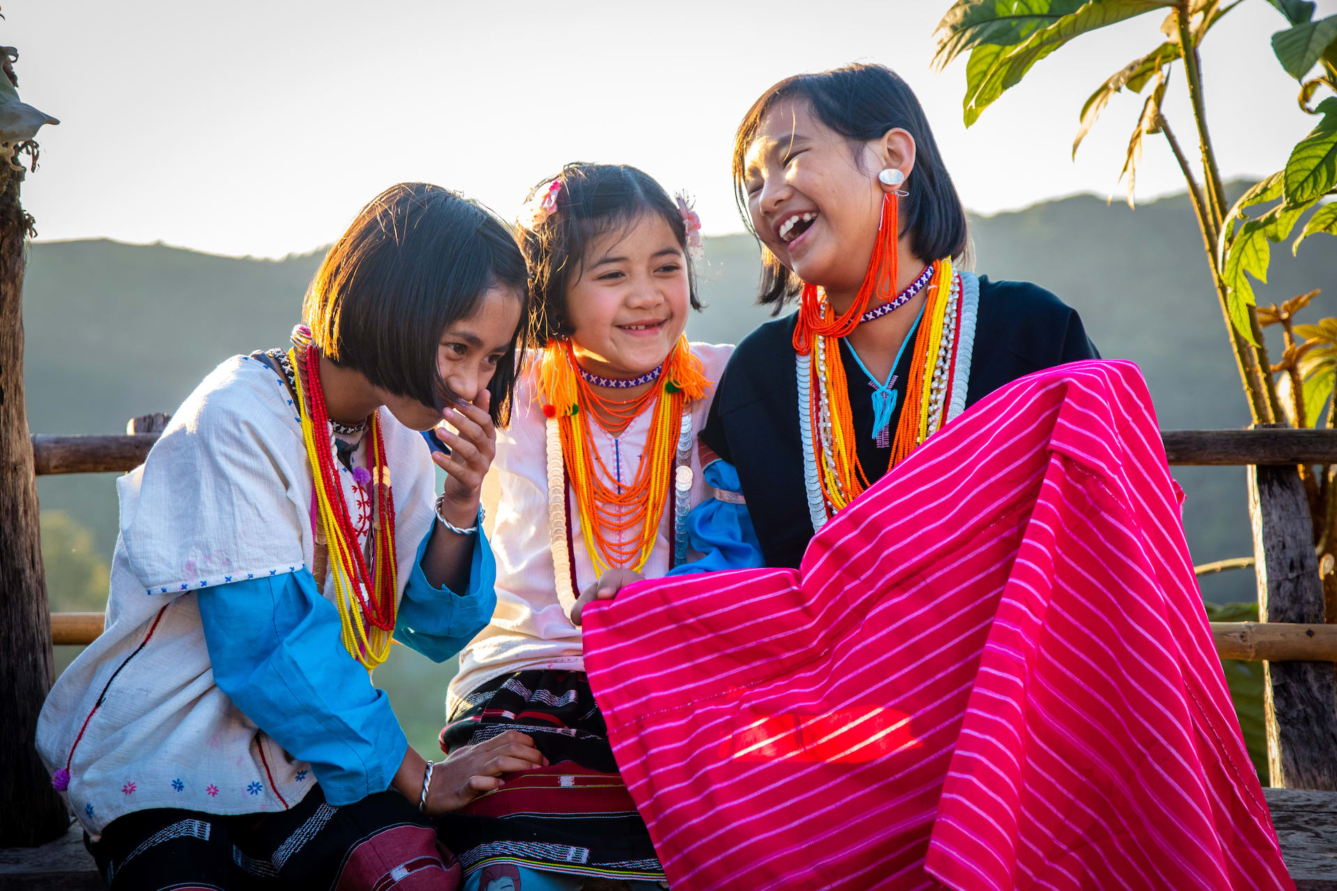 Three Thai girls sit together giggling.
