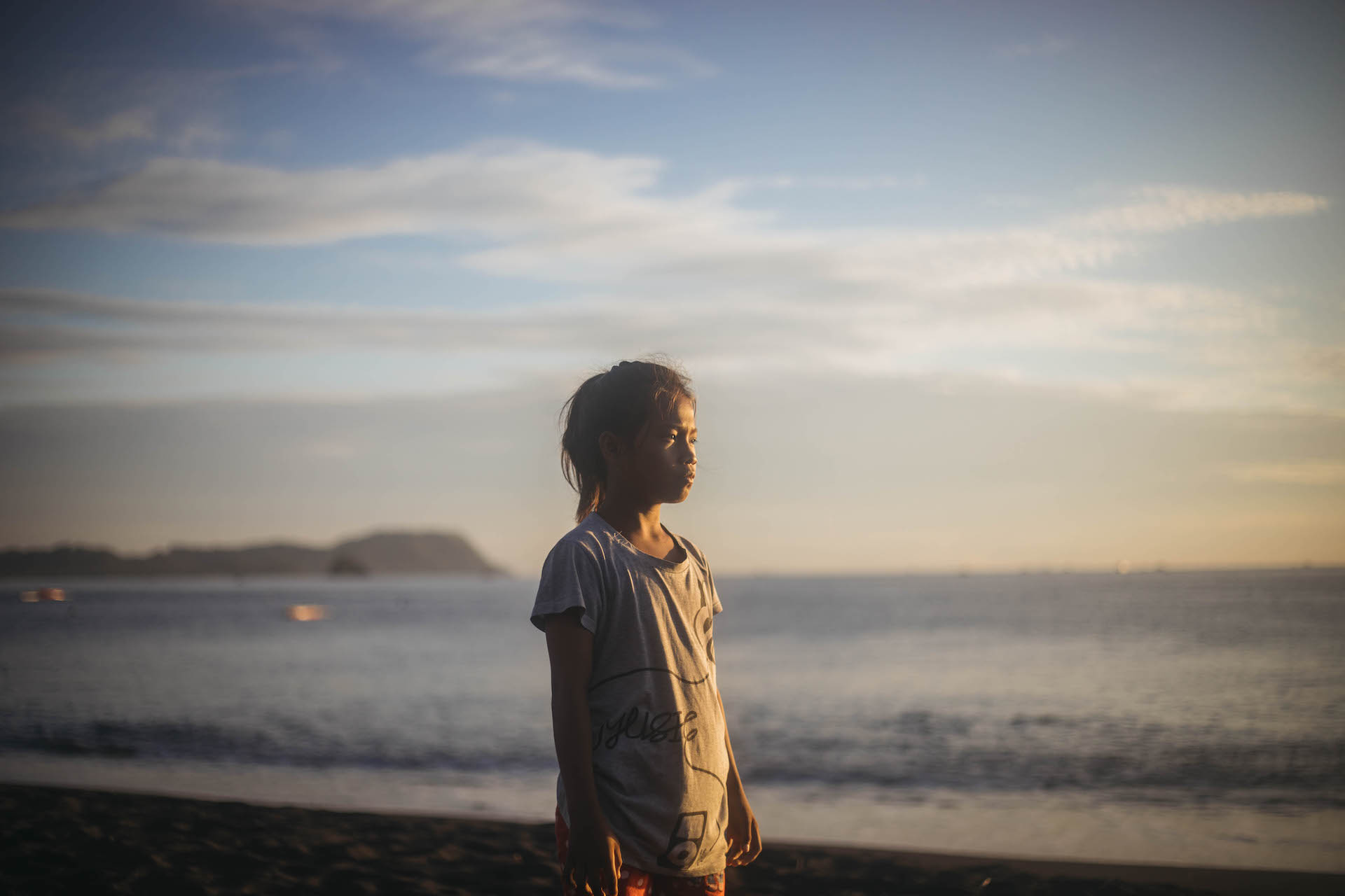 An Indonesian girl stands on a beach at sunset.
