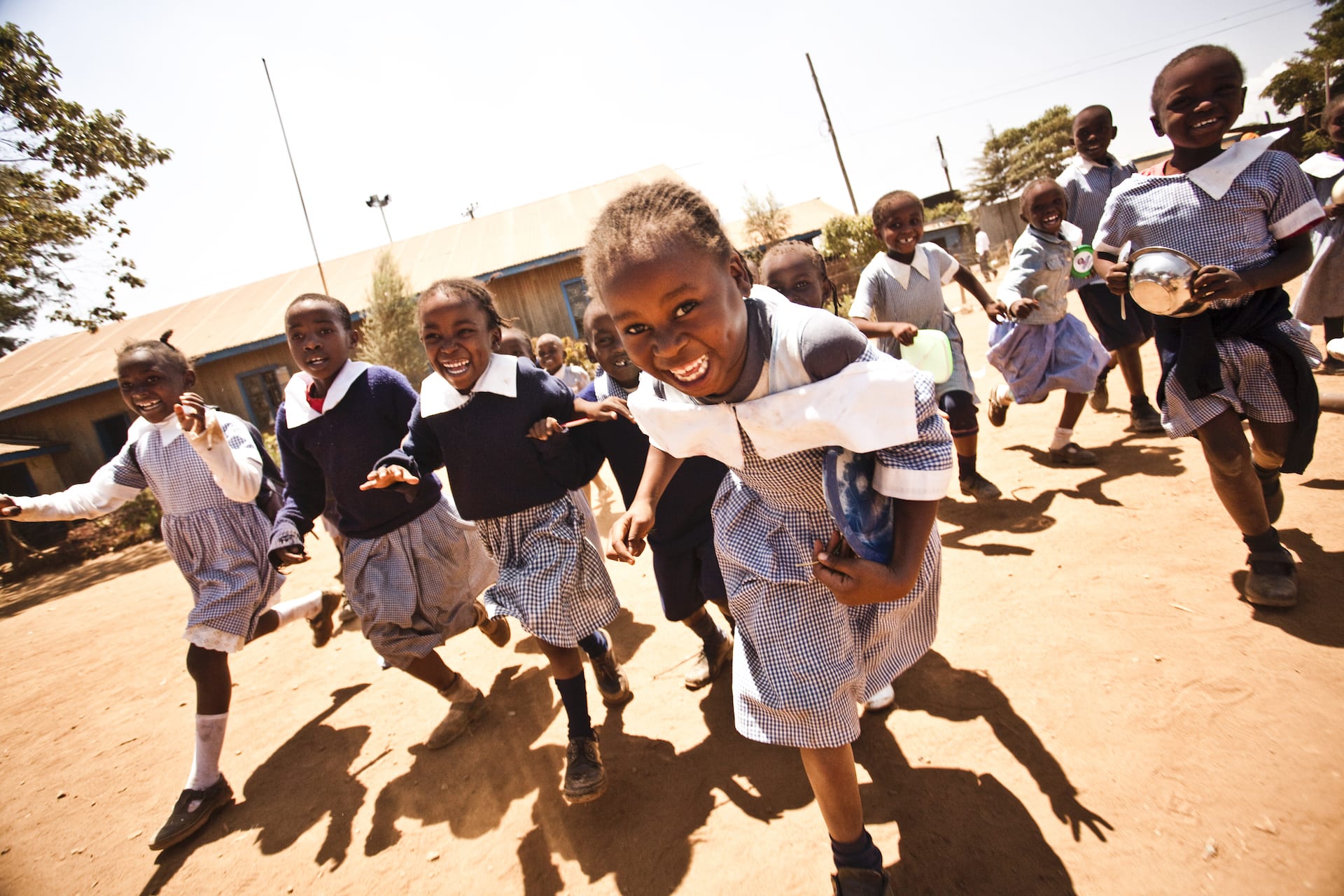Children smiling and running in a playground in Kenya.
