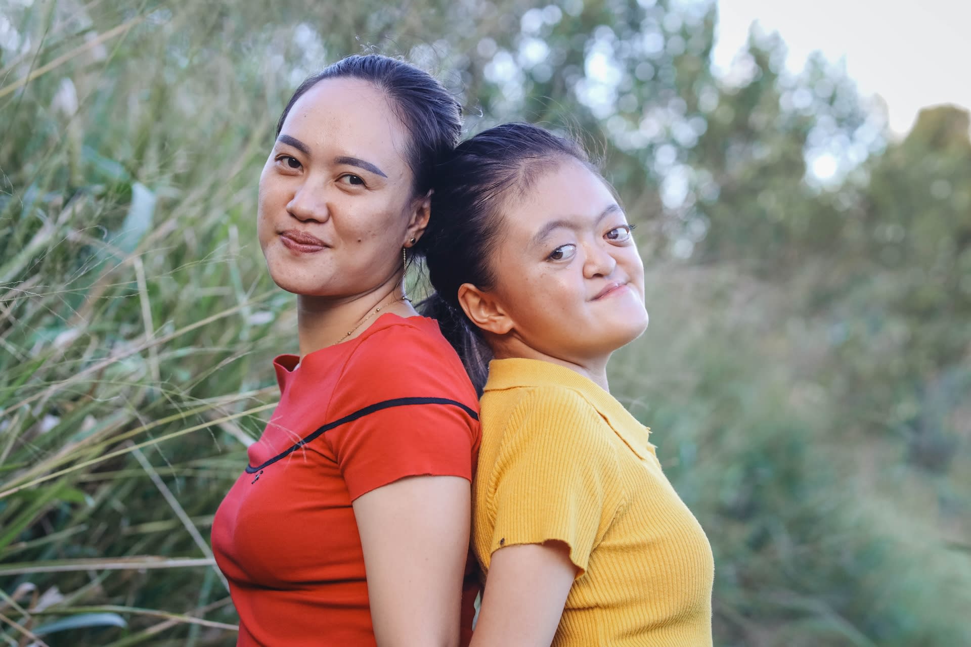 Karunia and her mother, Angel, stand back-to-back wearing red and yellow shirts. They look at the camera with smiles.
