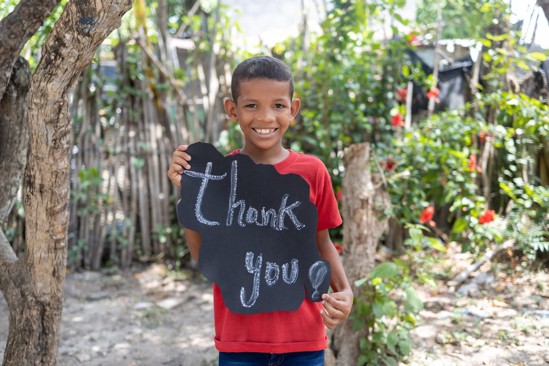 A Colombian boy named Franklin is smiling and holds up a sign that says "thank you!"