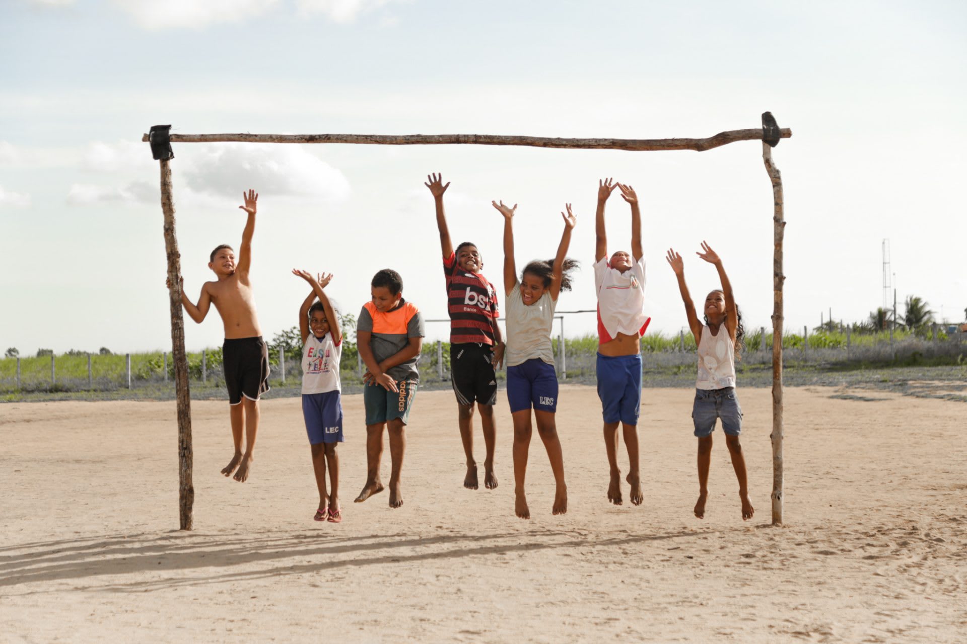 seven children jump up to reach a stick bar