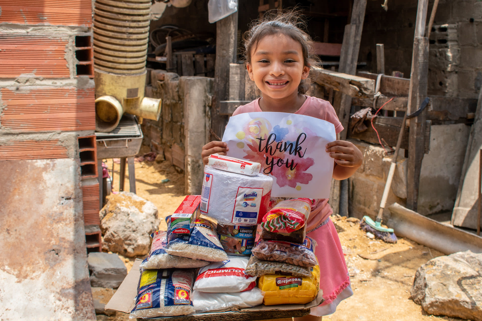 In Colombia, a girl holds a sign that says "Thank You", standing beside a grocery delivery from Compassion.