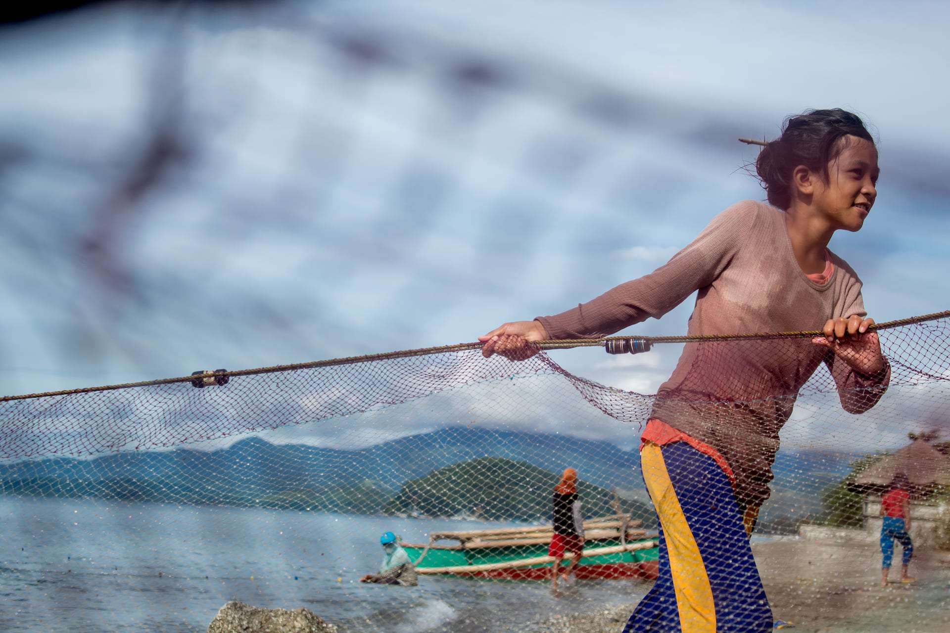 Ariane pulls a fishing net on the shore of the ocean.