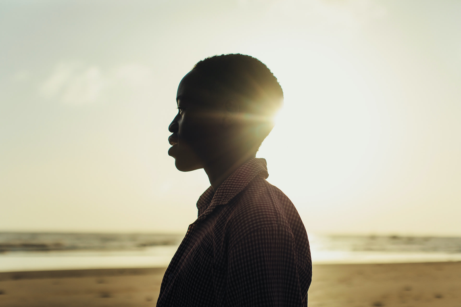 A silhouetted photo of a young Kenyan woman at sunset on a beach.