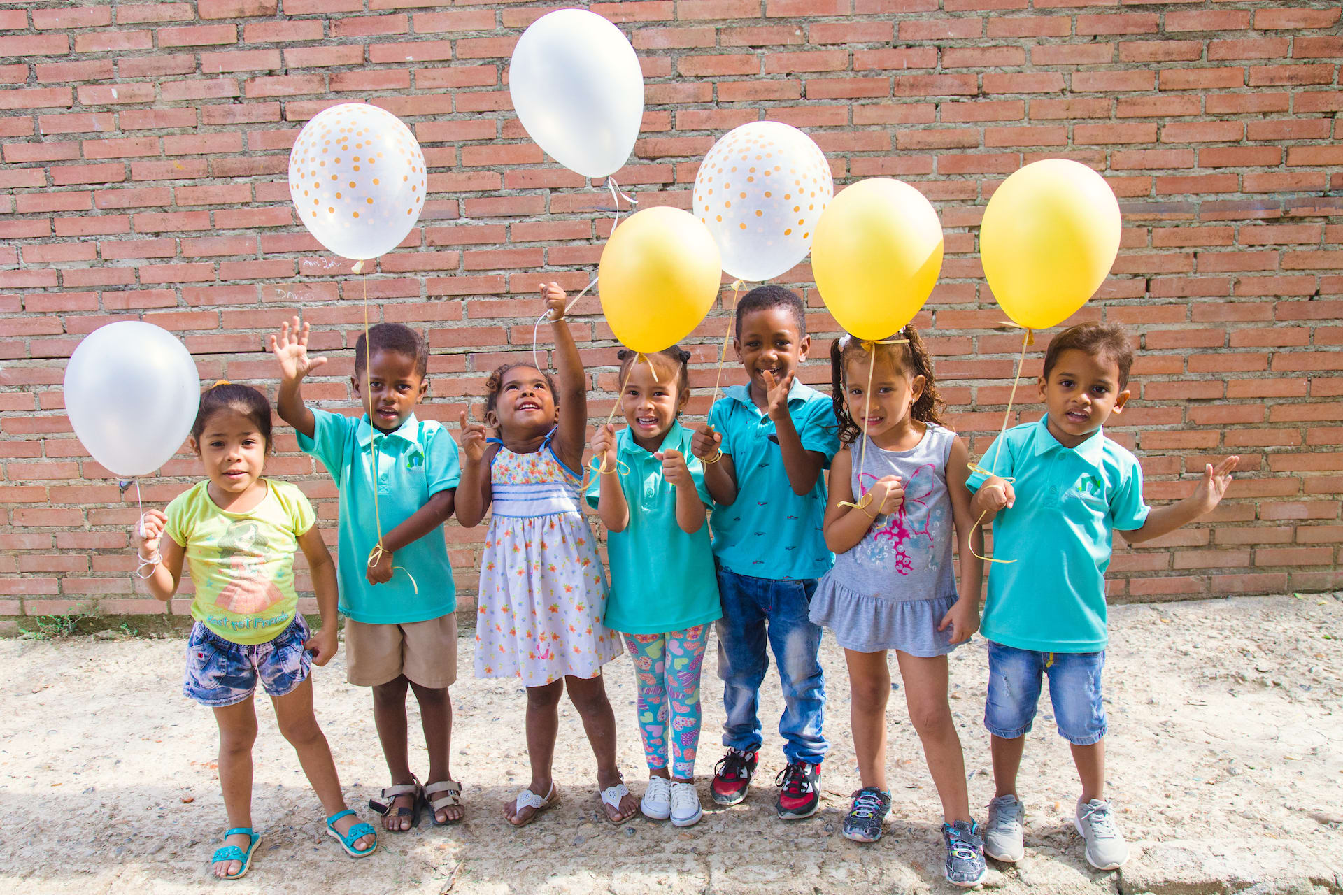 A group of children standing in a row holding yellow and white balloons.