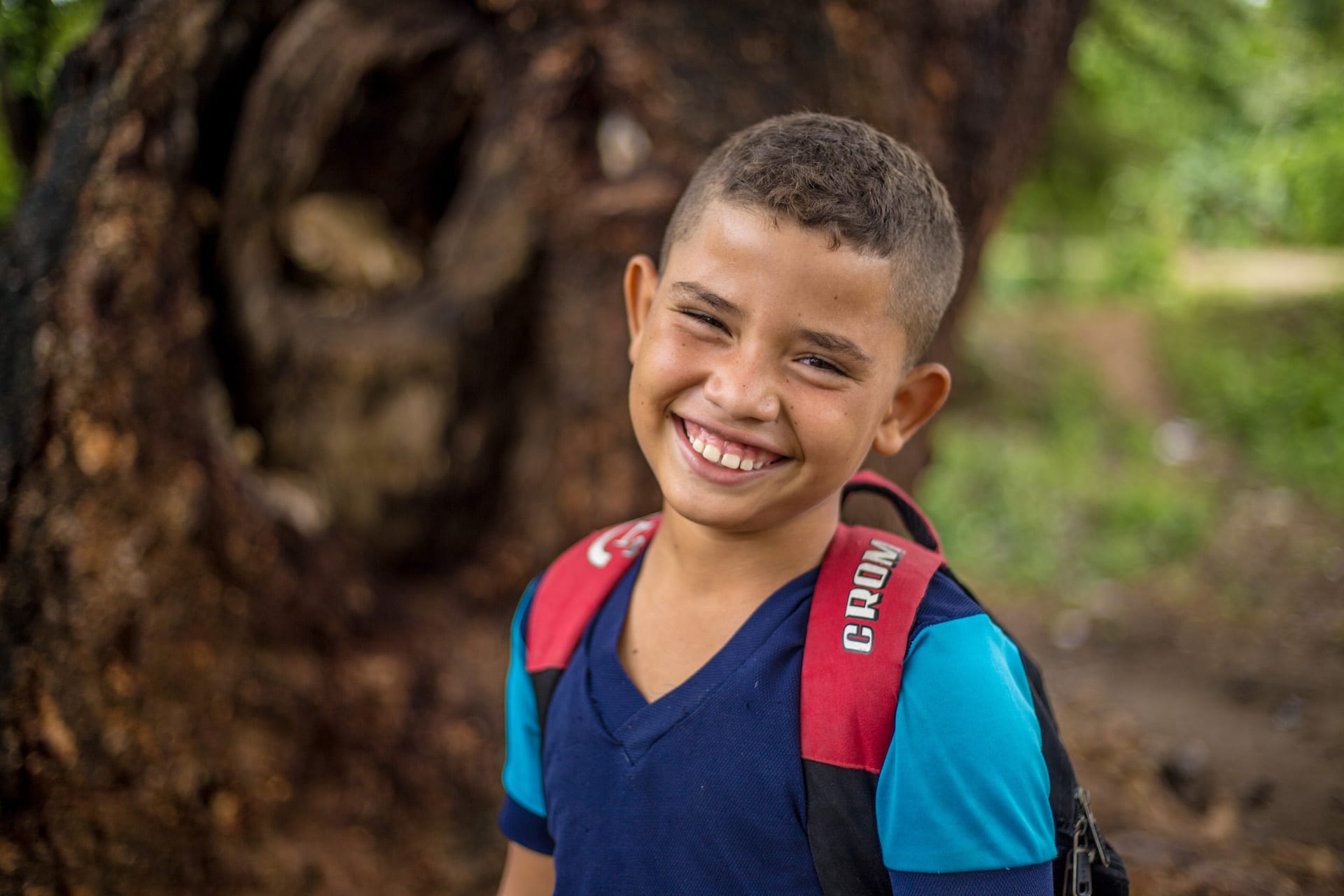 A boy smiles at the camera, wearing a backpack.
