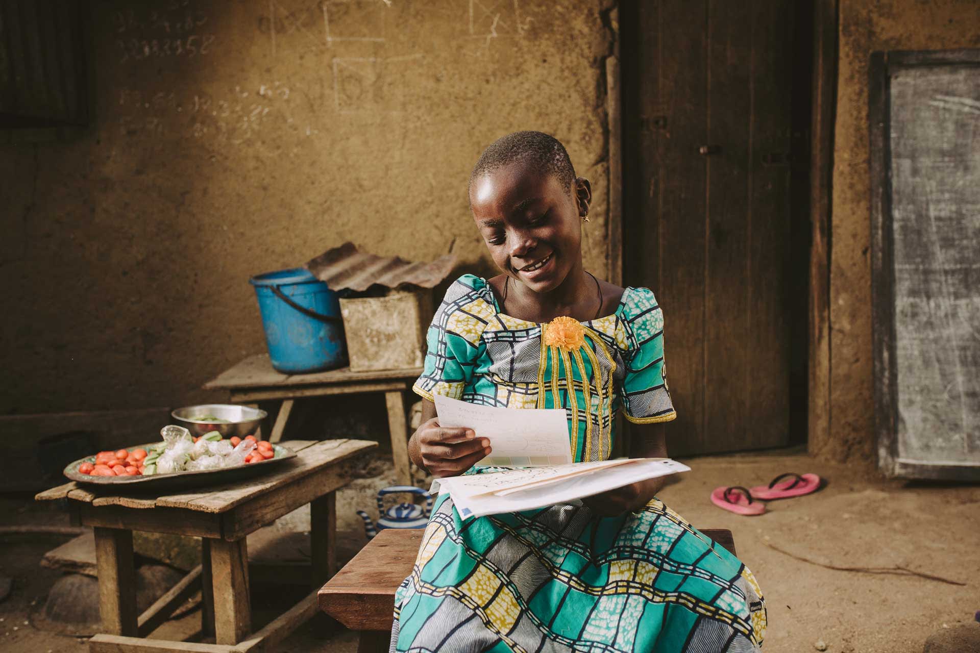 A young girl from Togo, in an ornate green dress, reads a letter from her sponsor.