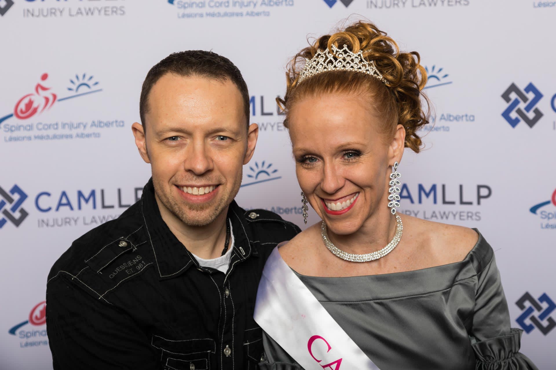 Vahen and her husband pose in front a red carpet backdrop at the Miss Wheelchair Canada awards. Vahen wheres a teirah and smlies at the camera.