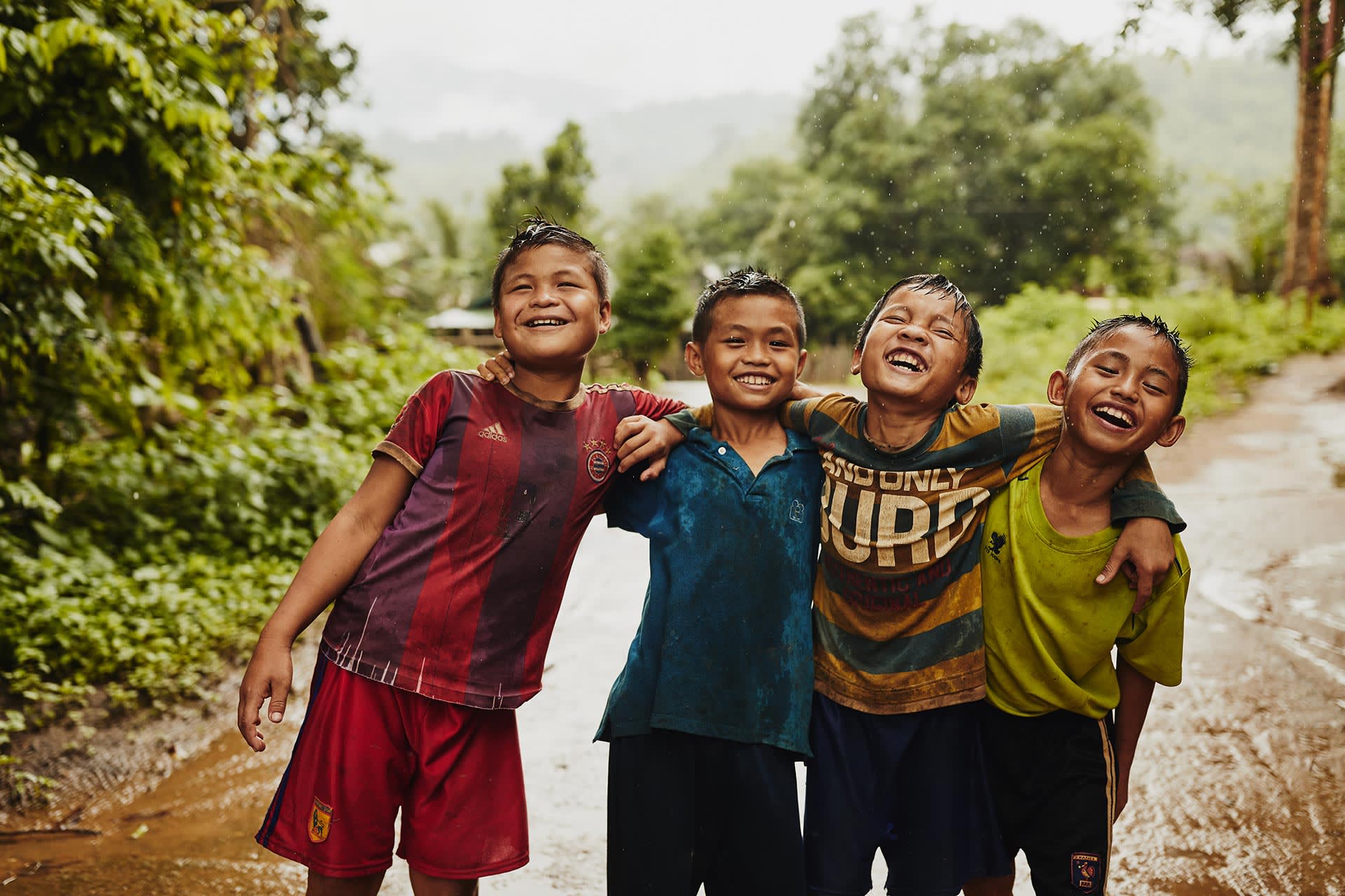 Four Thai thai boys stand in the rain and laugh together.