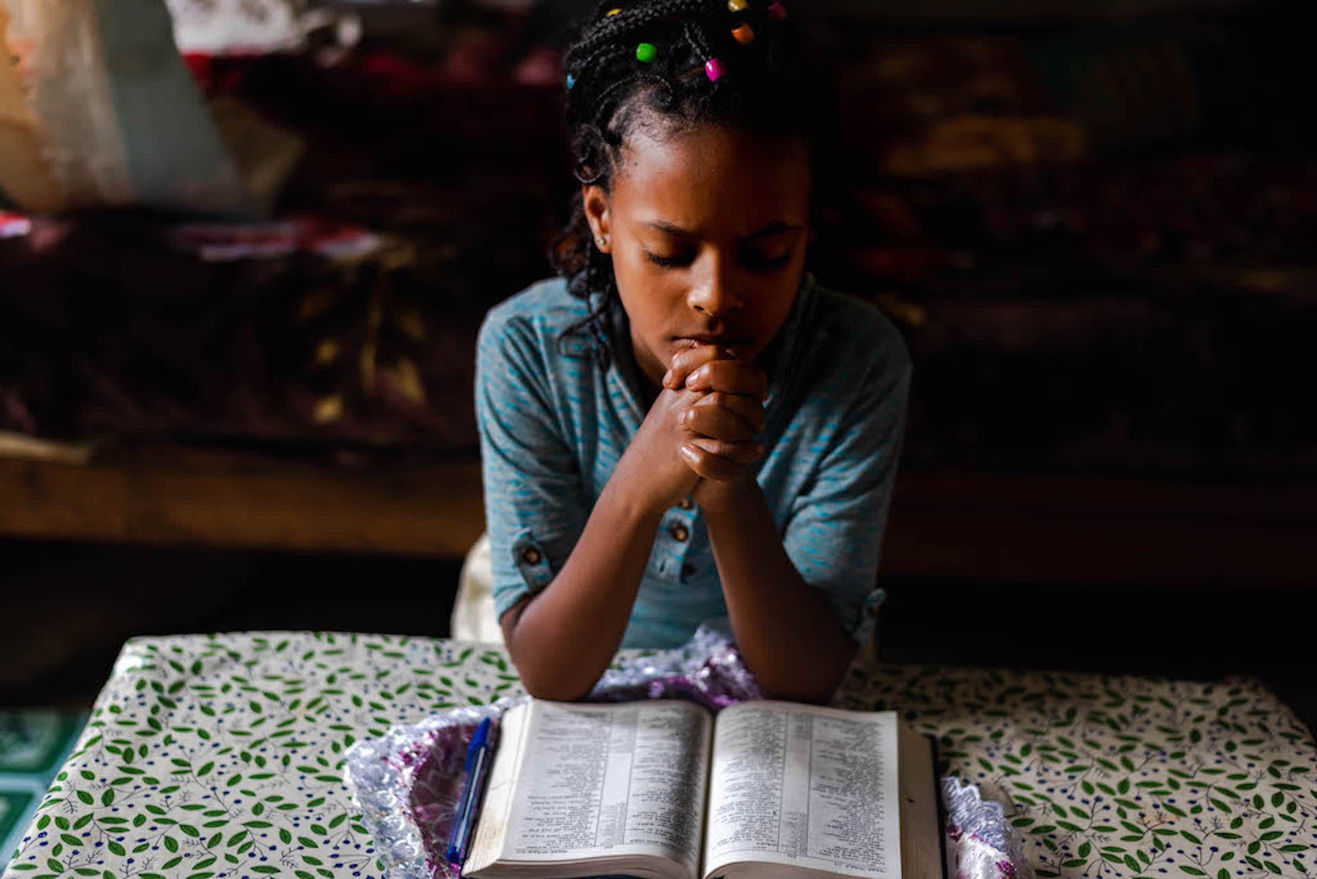 An Ethiopian girl praying with a Bible open on the table in front of her.