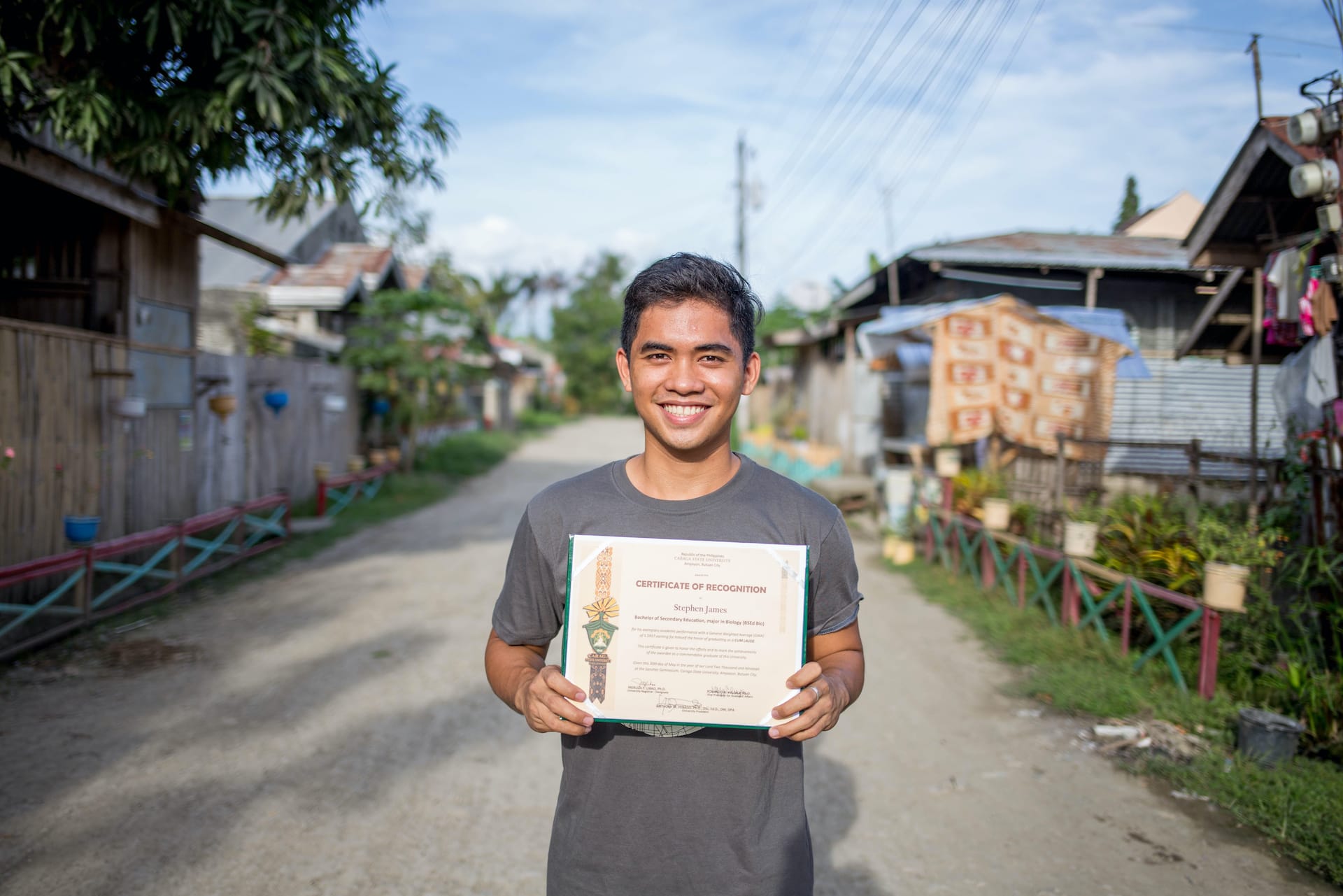 Stephen stands in the street, holding a certificate.
