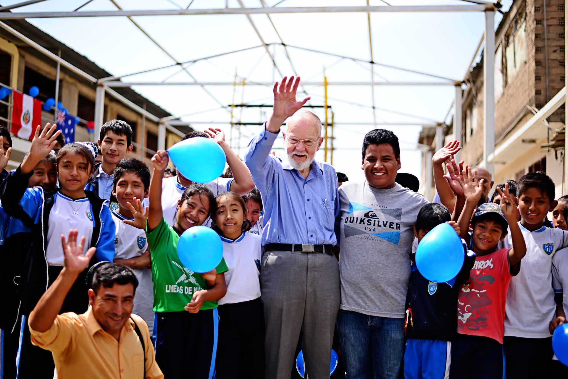 An older man stands at a child center surrounded by kids and leaders.