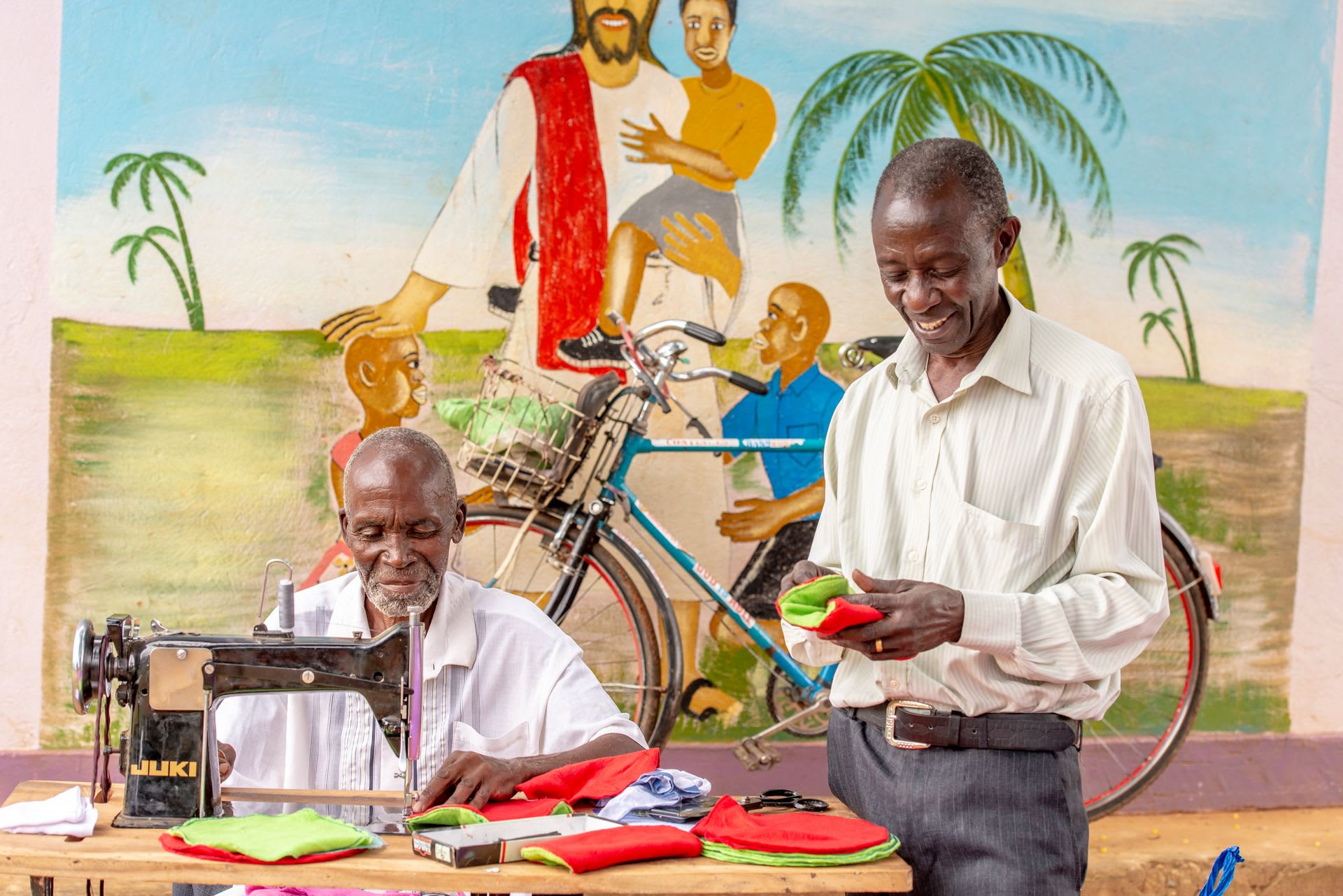 Two men at a table sewing sanitary pads.