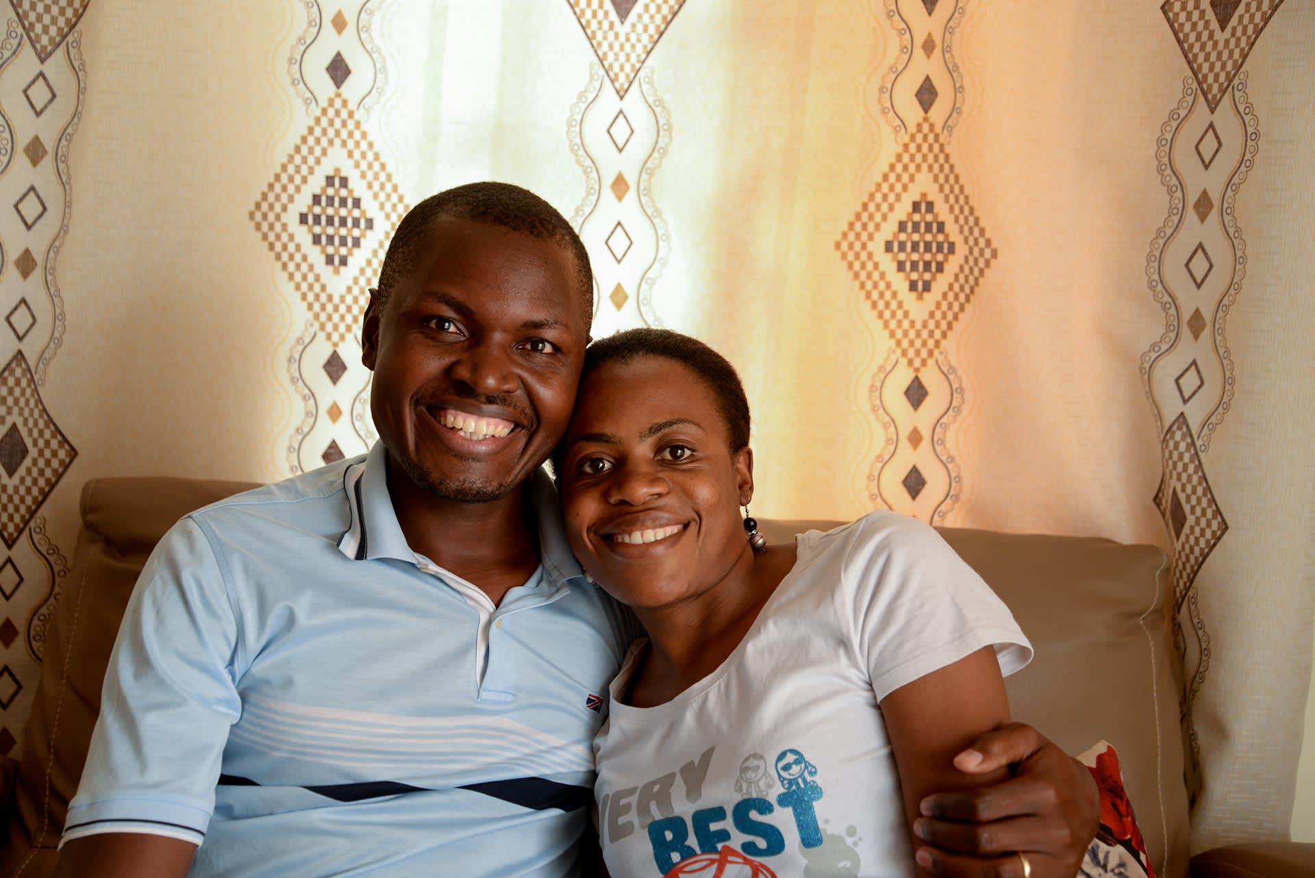 A Ugandan man and woman sit together on a couch and smile.