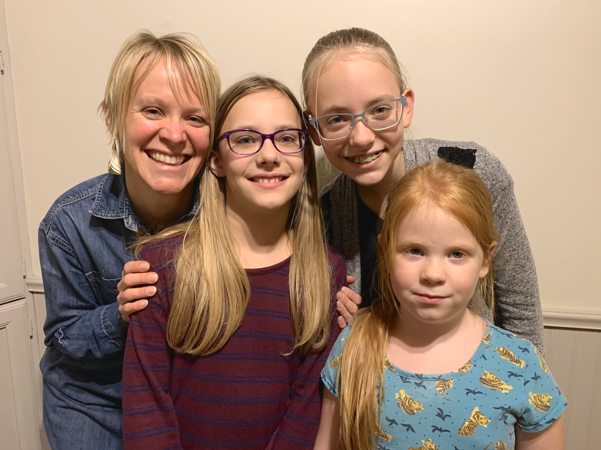 A mom and three girls smile together in their home.