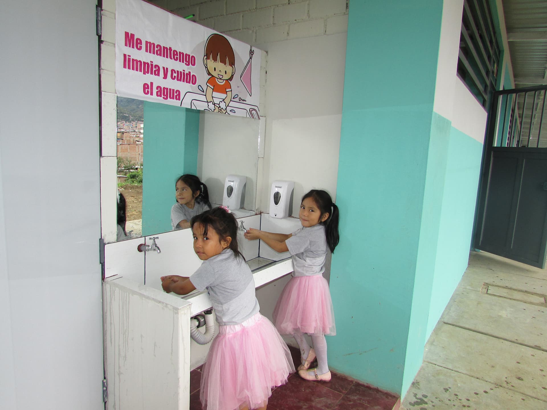 Two girls in pink dresses stand at the church sink and wash their hands