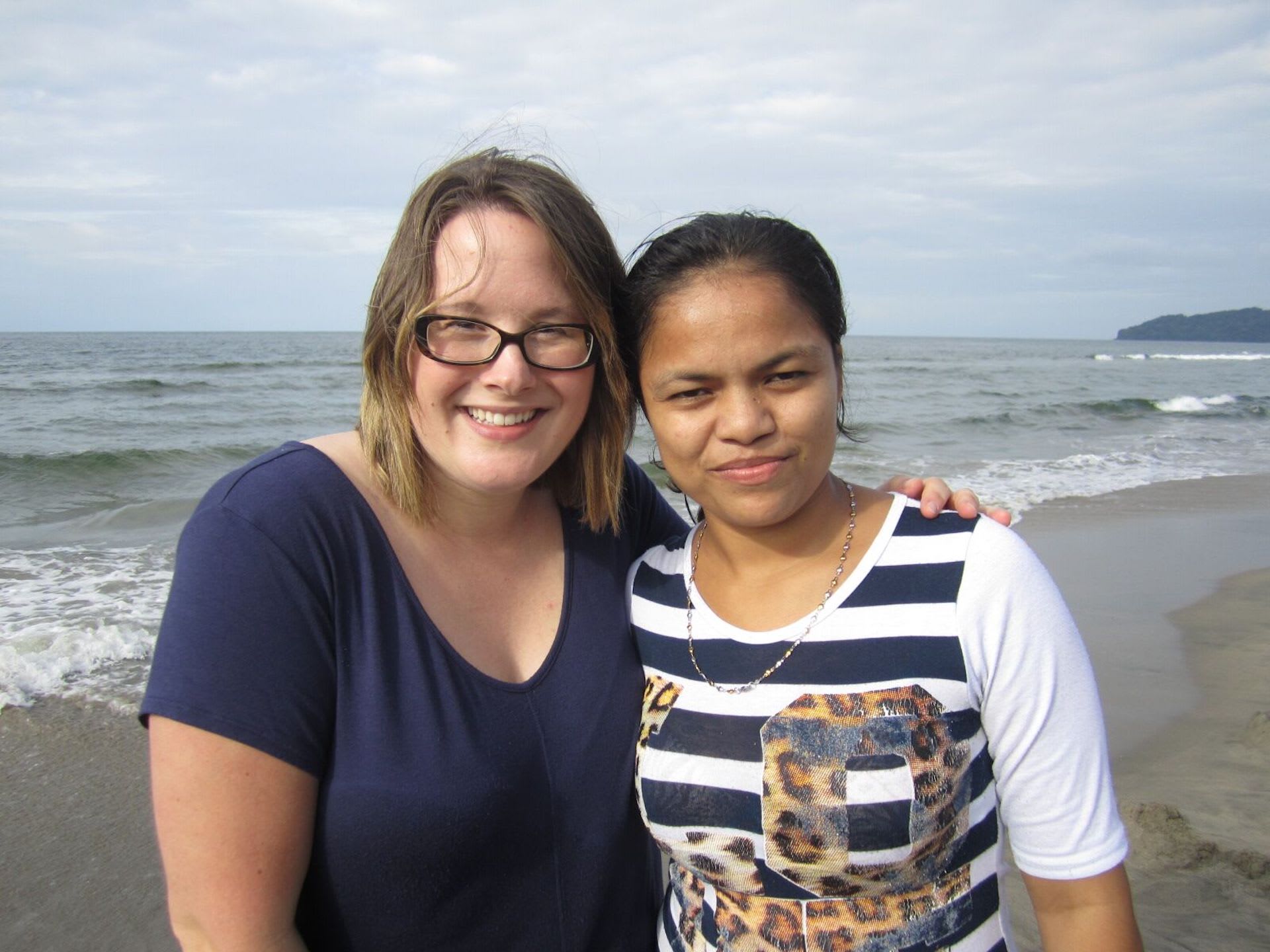Two women stand together on a beach.