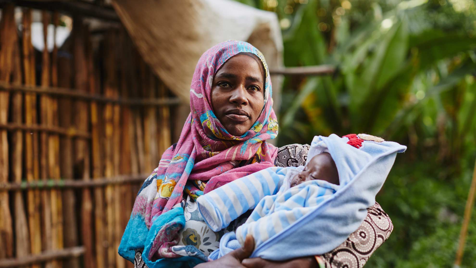 Woman wearing pink and blue holds her swaddled baby.